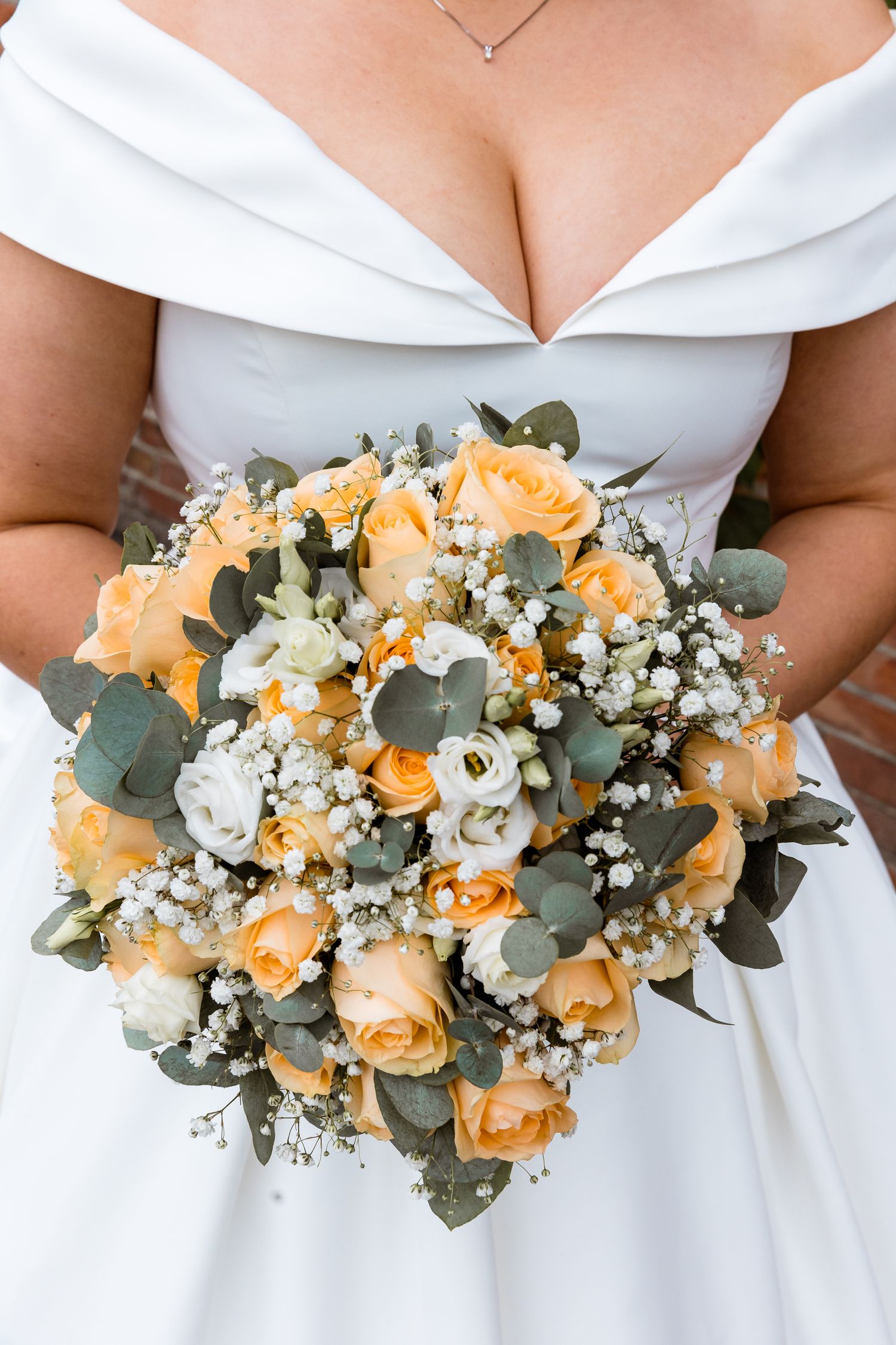 A stunning bridal bouquet with peach roses, white baby's breath, and eucalyptus leaves against a white dress.