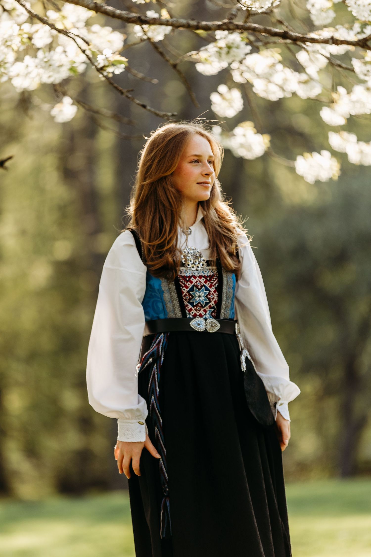 Person in traditional embroidered dress twirls in sunlit garden setting.