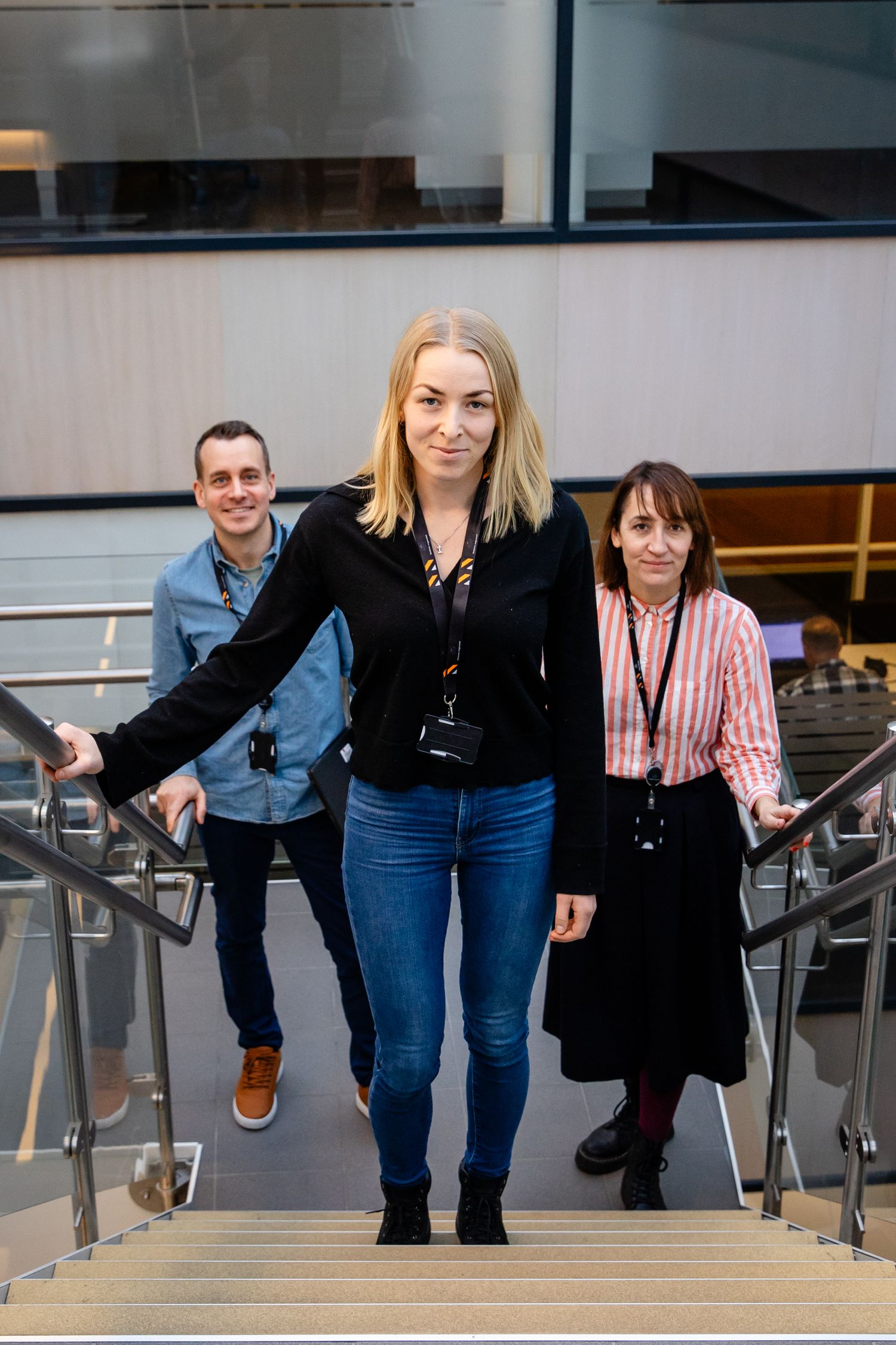 People descending modern staircase with glass and metal railings in office building.