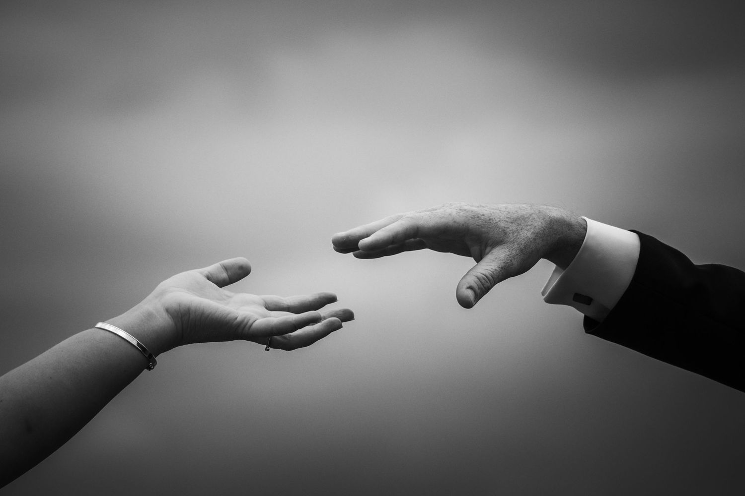 Artistic black and white photo of hands reaching towards each other against a gradient background.