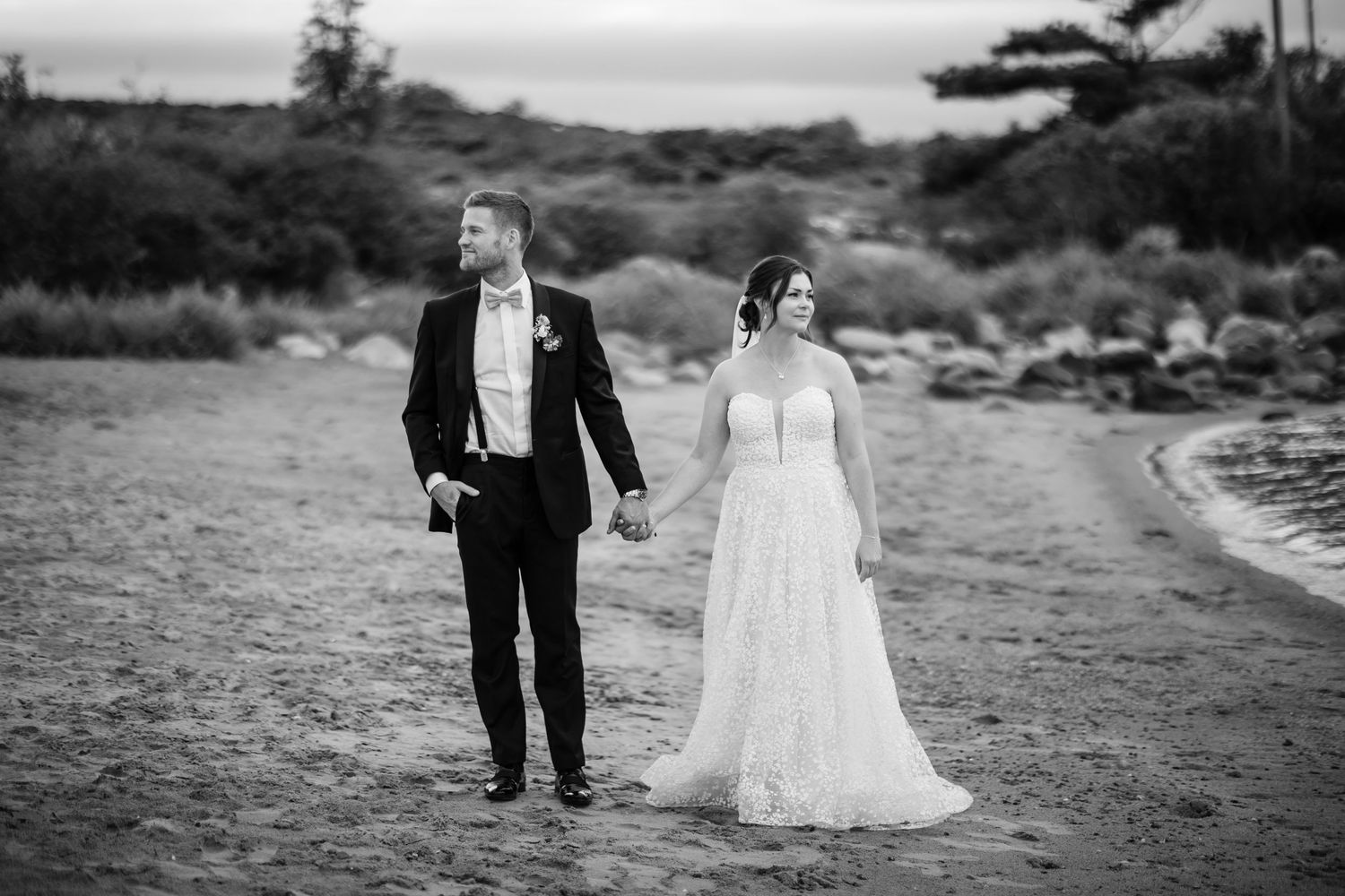 Black and white wedding photo of a couple walking together on a coastal path.