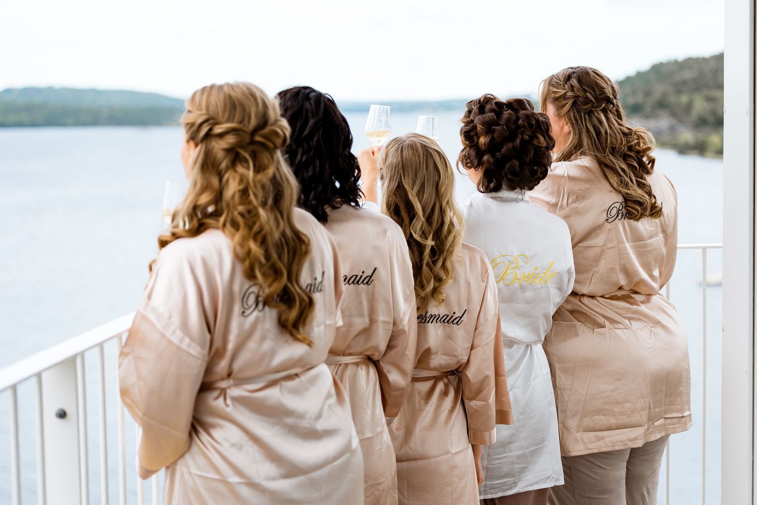Bridesmaids in matching robes looking out over a waterfront view.