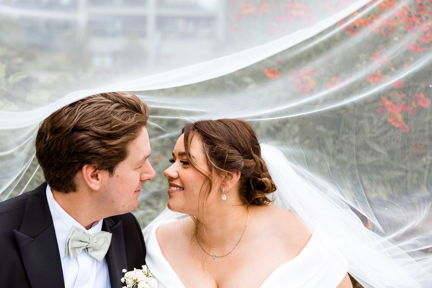 An intimate moment between newlyweds under a flowing veil with soft lighting.