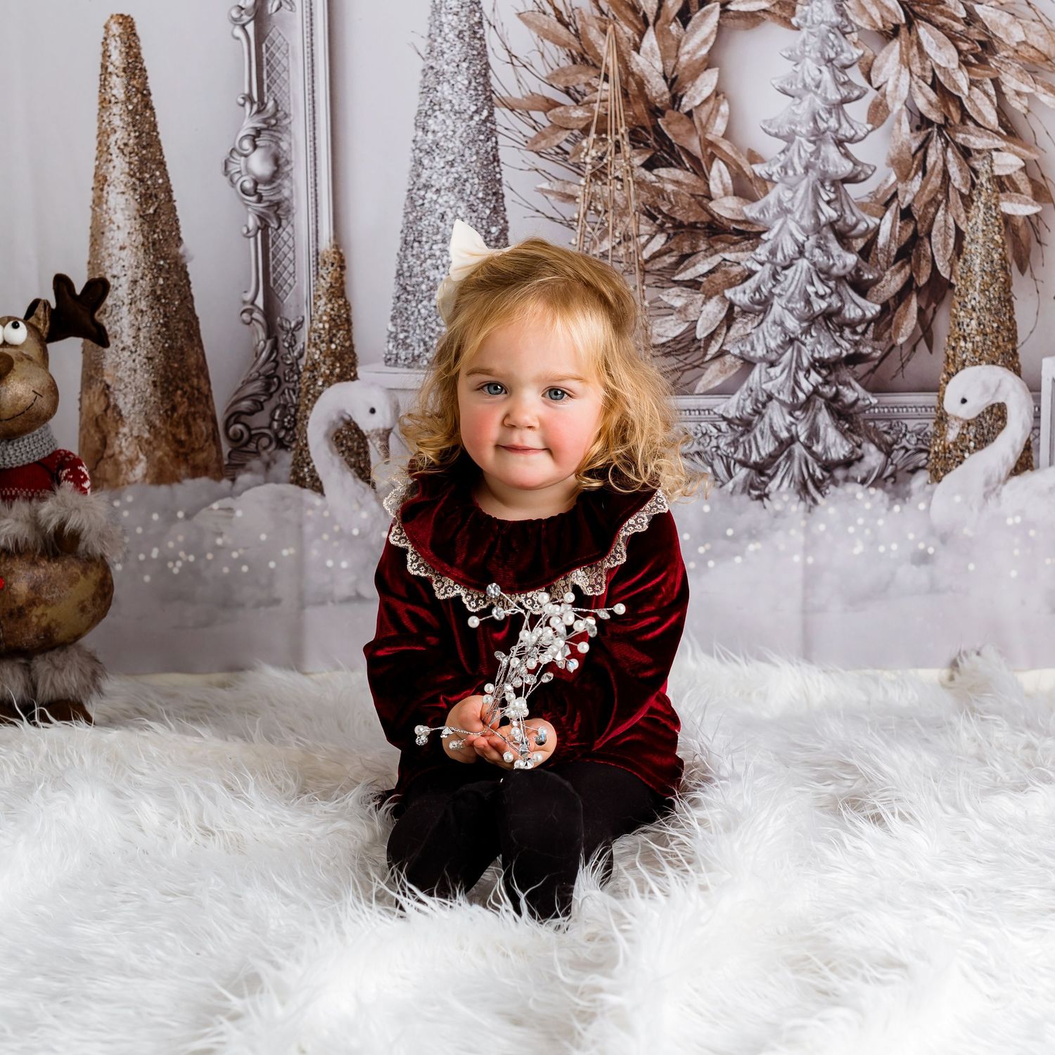 Winter wonderland photo session with red velvet dress against snowy white backdrop and silver trees.