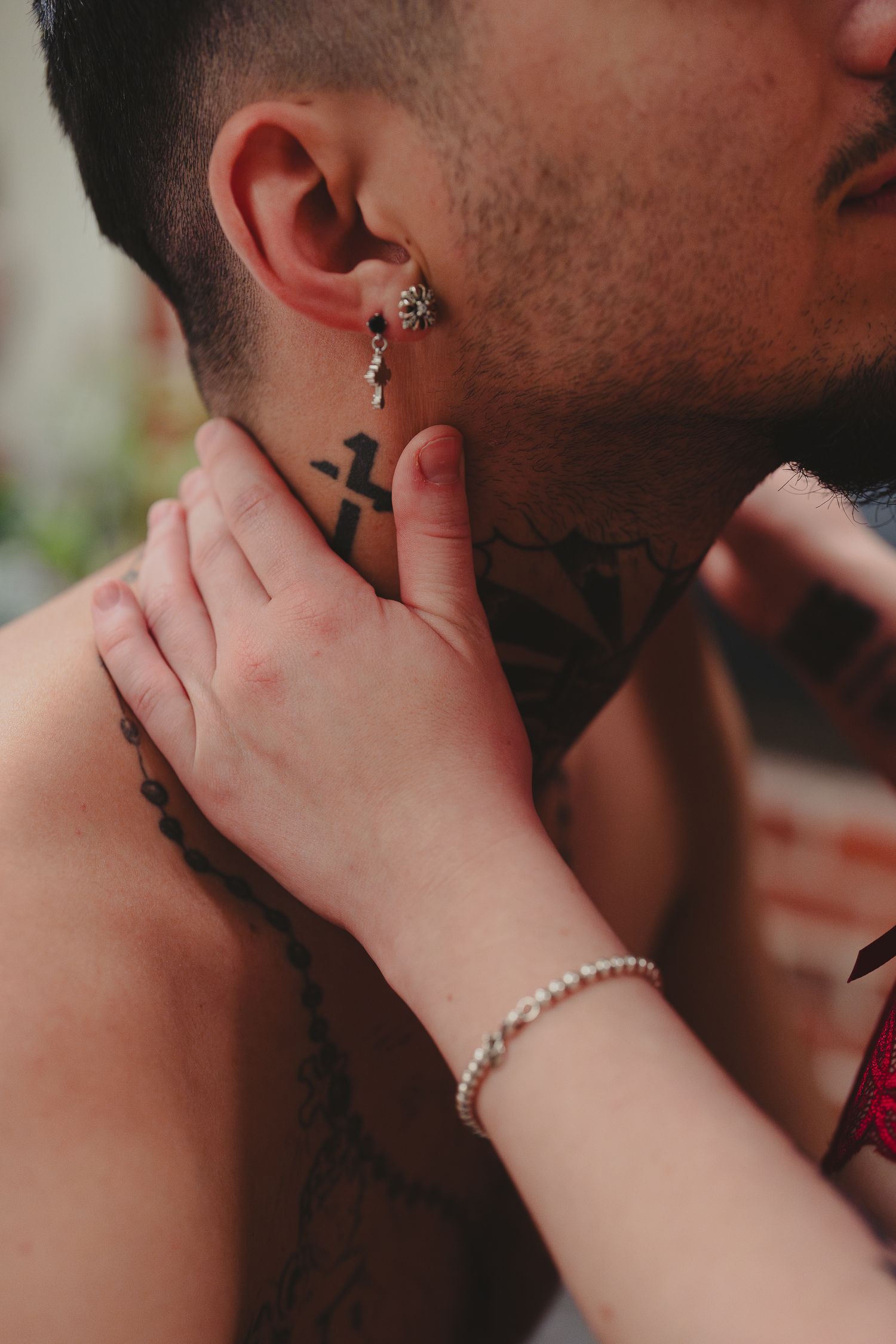 Close-up of tattooed man's neck and ear with partner's hand gently touching his face.