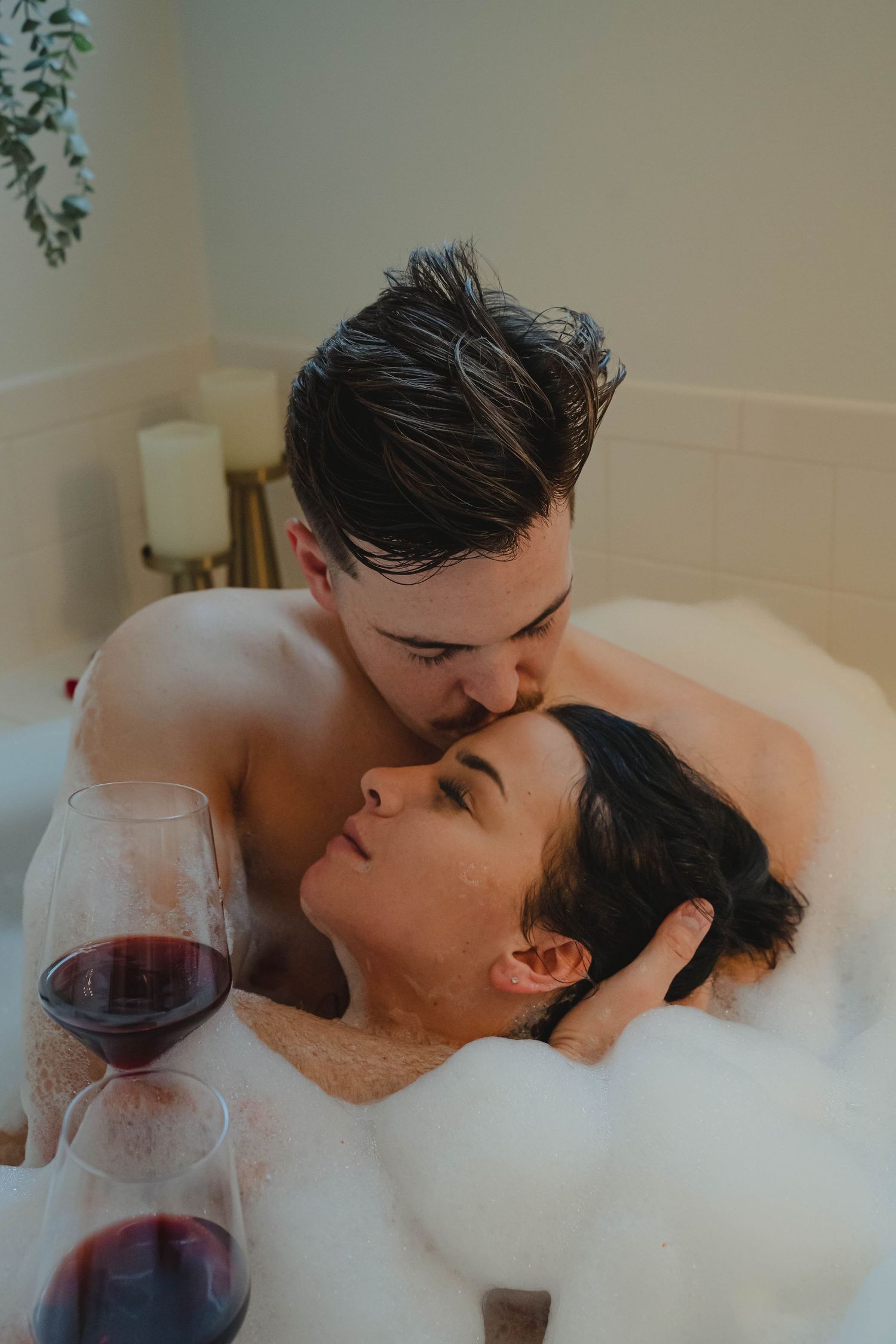 Couple sharing a romantic moment in a bubble bath with red wine glasses nearby.
