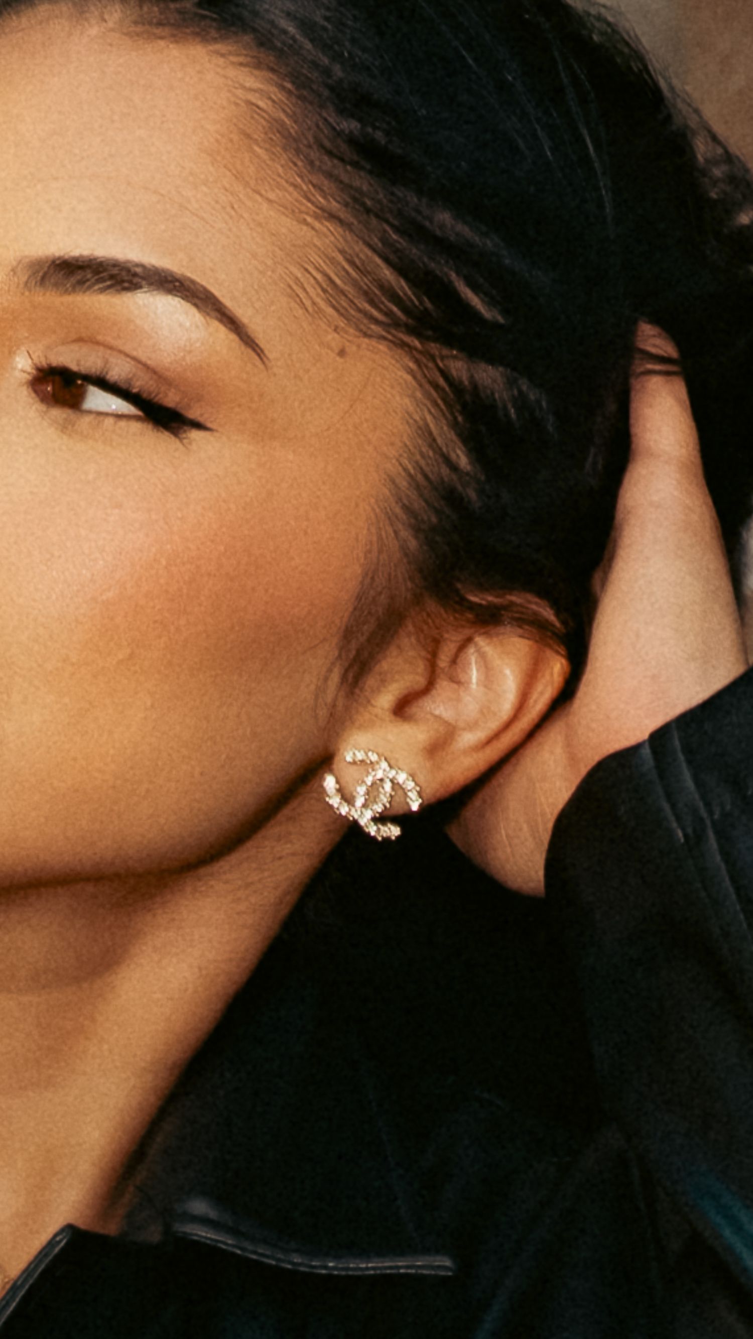 Close-up portrait of a woman wearing a sparkling Chanel CC logo stud earring.