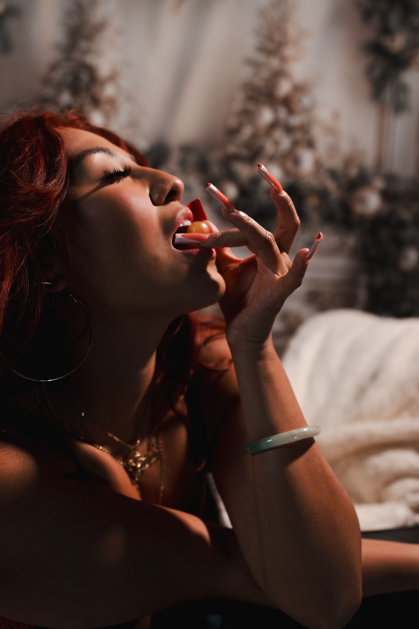 Woman with red hair and hoop earrings posing dramatically in moody sunlit room.