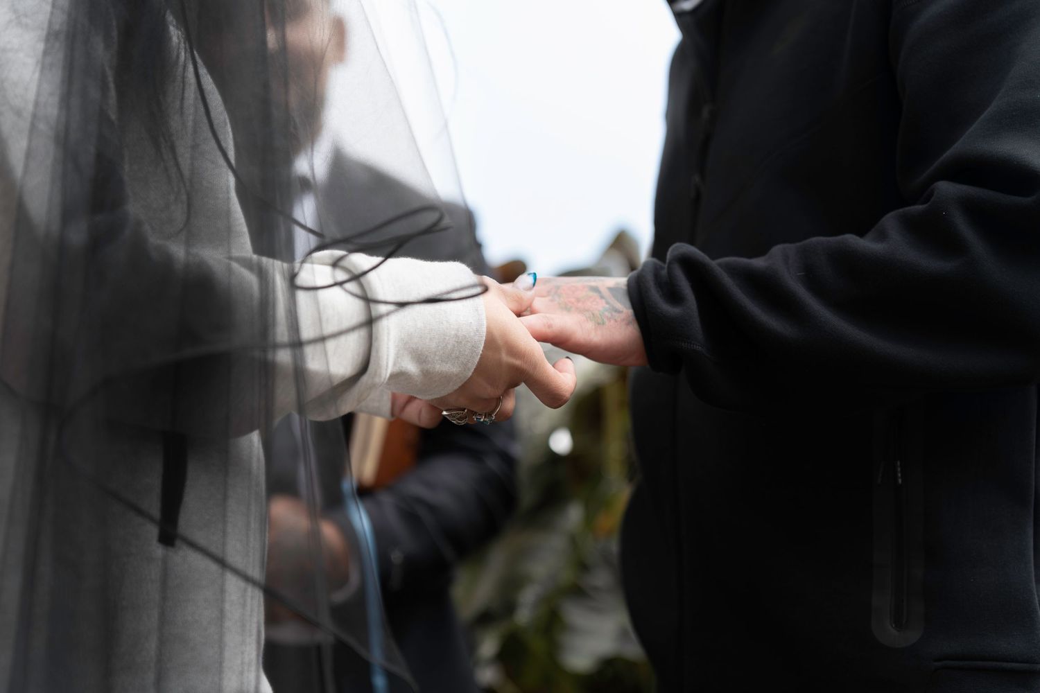 Bride and groom holding hands gently through a sheer wedding veil outdoors in Salem, Oregon.