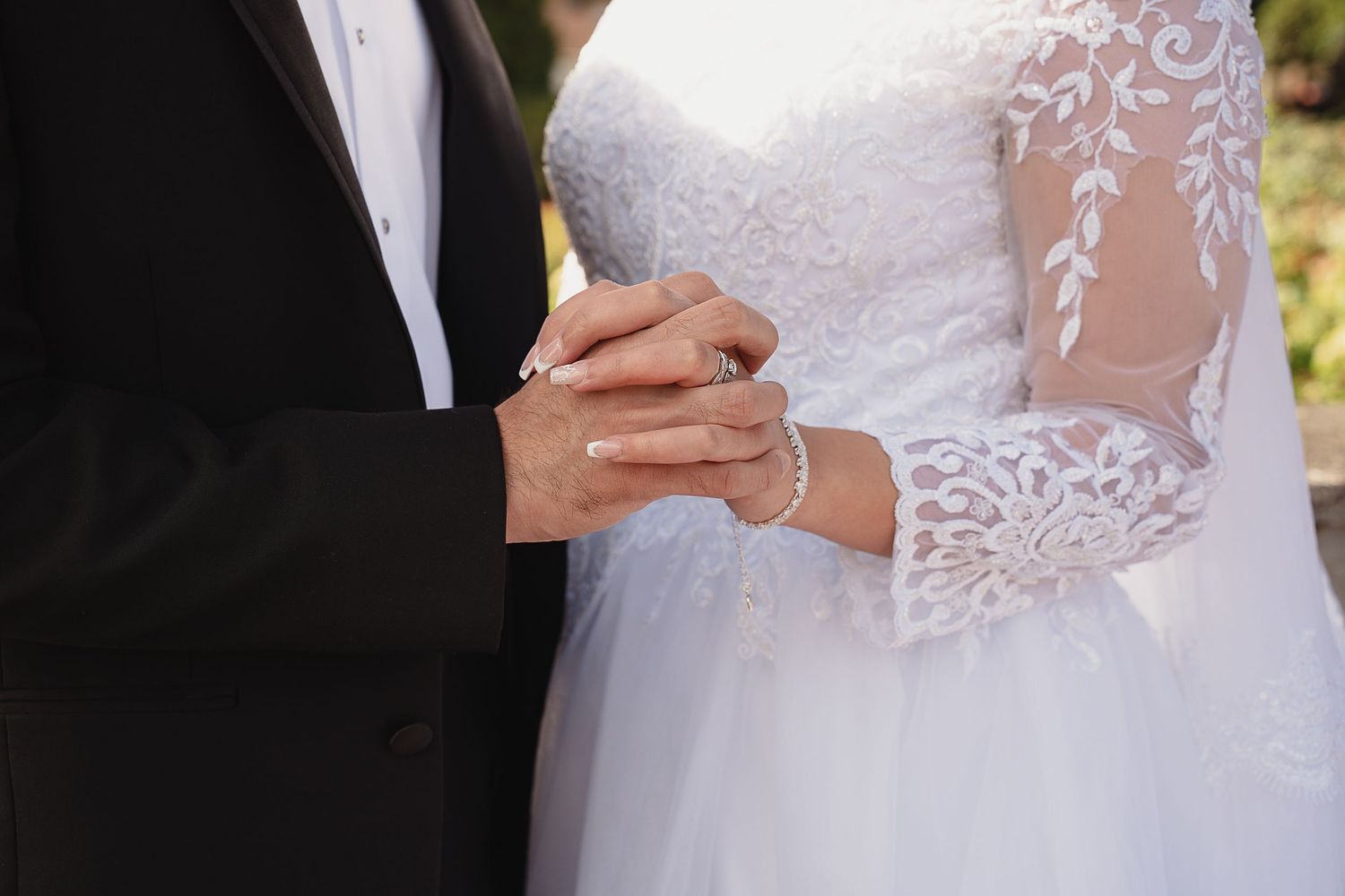 Close-up of bride and groom holding hands, showcasing lace wedding dress sleeve and pearl bracelet in Beaverton, Oregon.