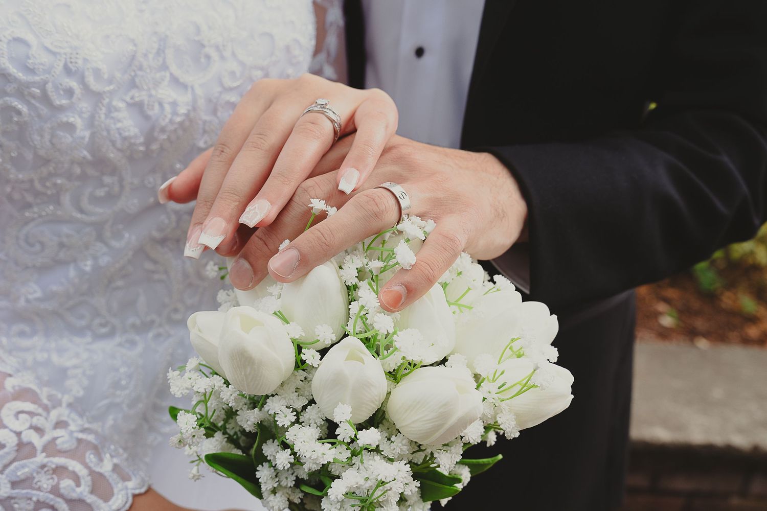 Newlyweds display wedding rings over a bouquet of white tulips and baby's breath.