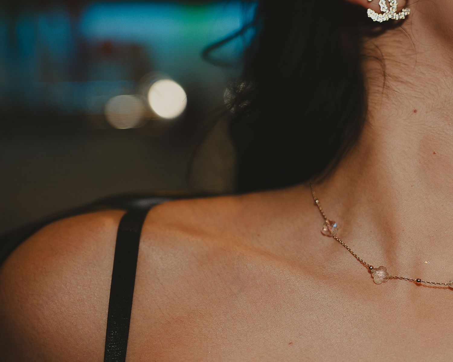 Close-up of a woman's neckline featuring a delicate gold chain necklace and a floral hair accessory.