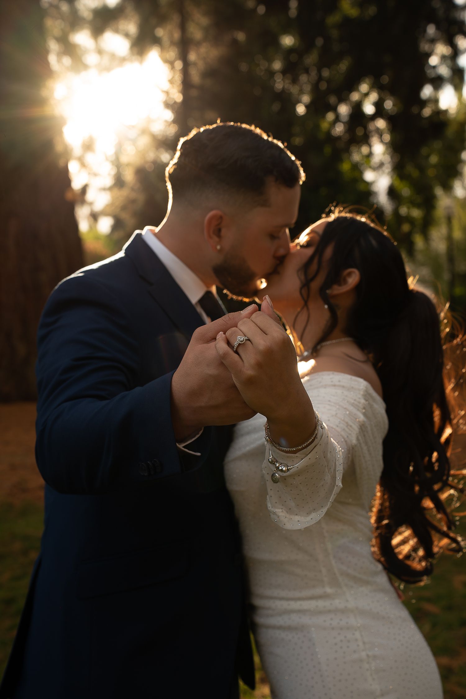 Bride and groom sharing a tender kiss at sunset in a forest, showcasing diamond engagement ring in Beaverton, Oregon.