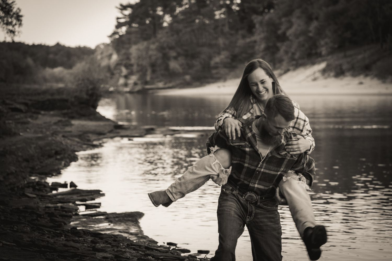 Wisconsin Couple and Engagement Photographer - Couple laughing on riverbank in fall during engagement session in Wisconsin during sunset.