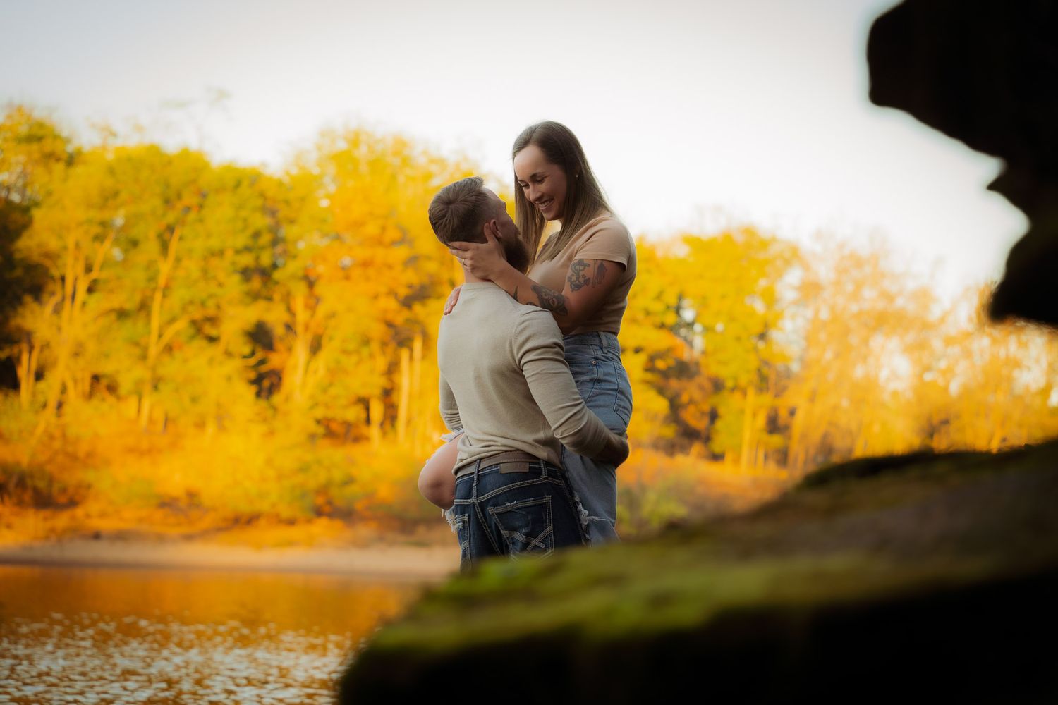 Wisconsin Couple and Engagement Photographer - Couple smiling on riverbank in fall during an engagement session in Wisconsin during sunset.