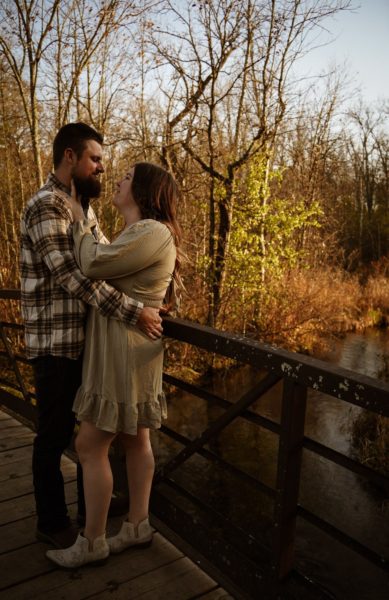 Wisconsin Couple and Engagement Photographer - Couple smiling on bridge in woods in fall during an engagement session during sunset.