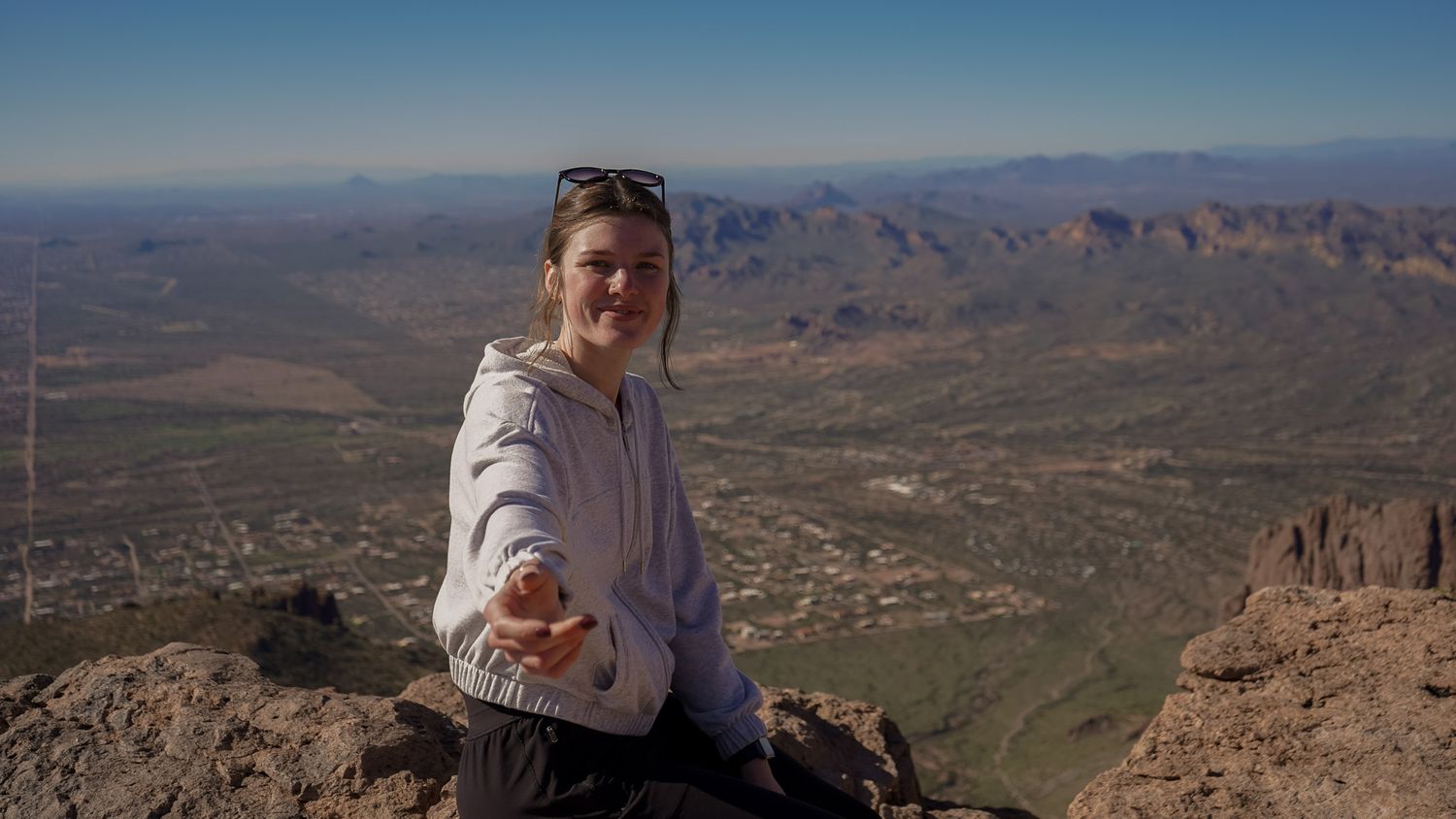 Wisconsin Portrait and Lifestyle Photographer - Beautiful woman sitting on a mountain in Arizona in the sun with hand reaching out.