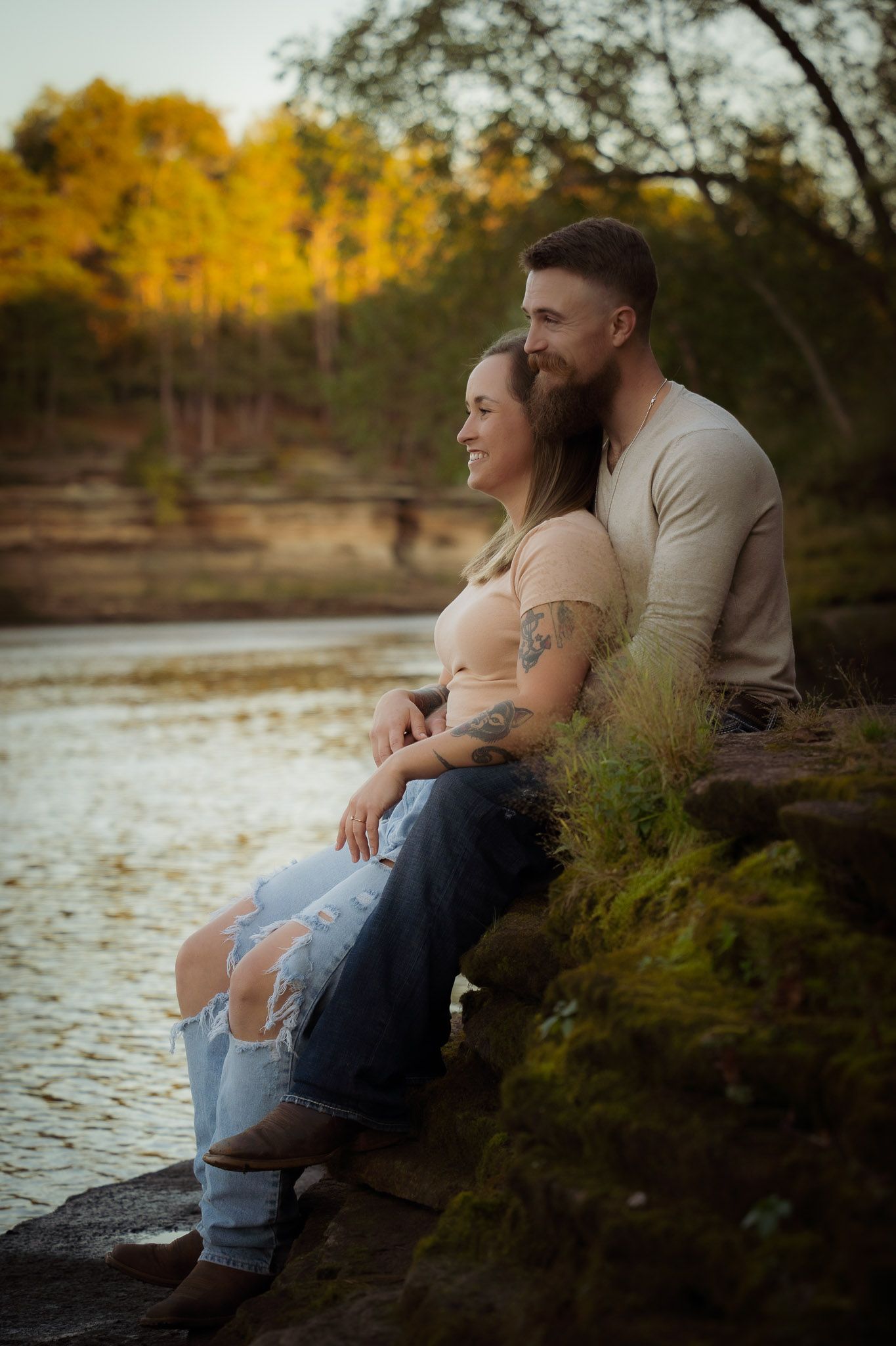Wisconsin Couple and Engagement Photographer - Couple smiling on riverbank in fall during an engagement session in Wisconsin during sunset.