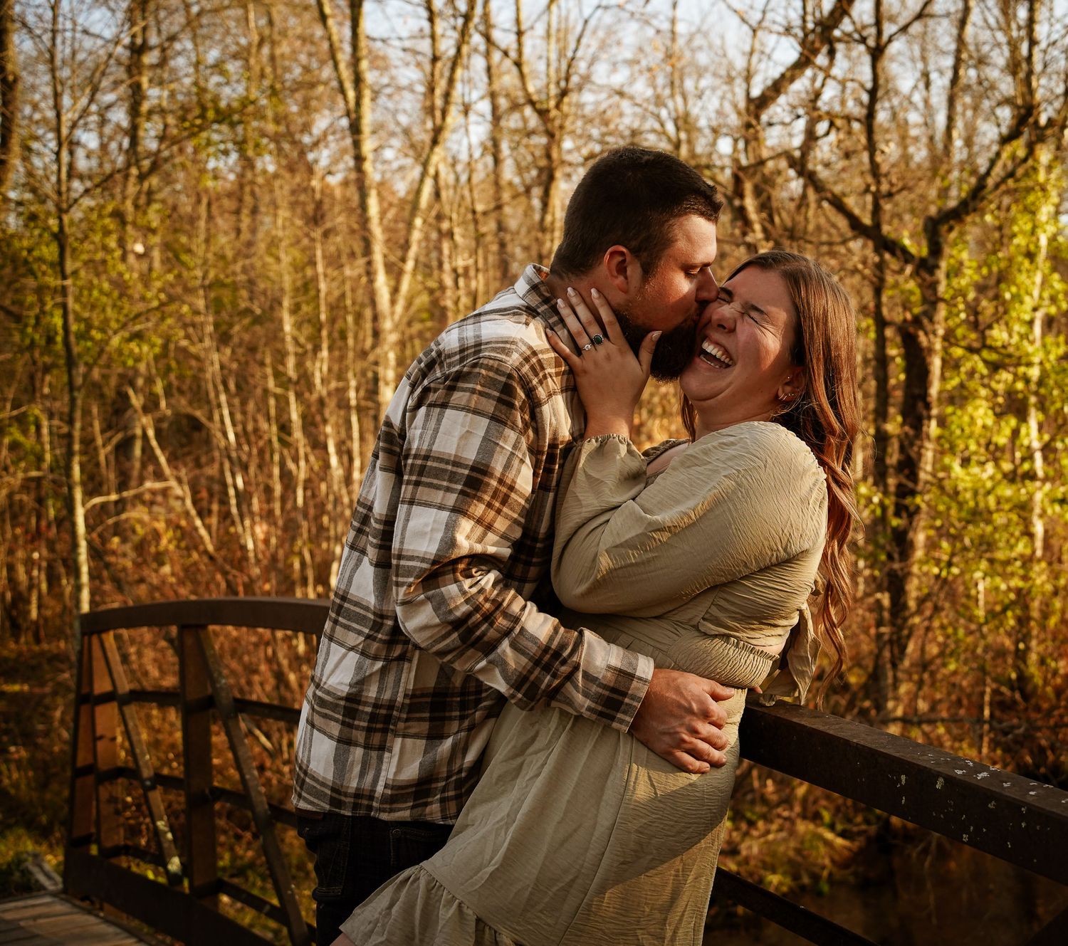 Wisconsin Couple and Engagement Photographer - Couple kissing on bridge in woods in fall during an engagement session during sunset.