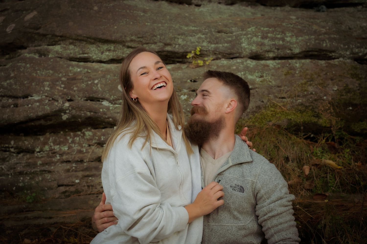 Wisconsin Couple and Engagement Photographer - Couple smiling in fall during an engagement session in Wisconsin during sunset by cliff/rocks