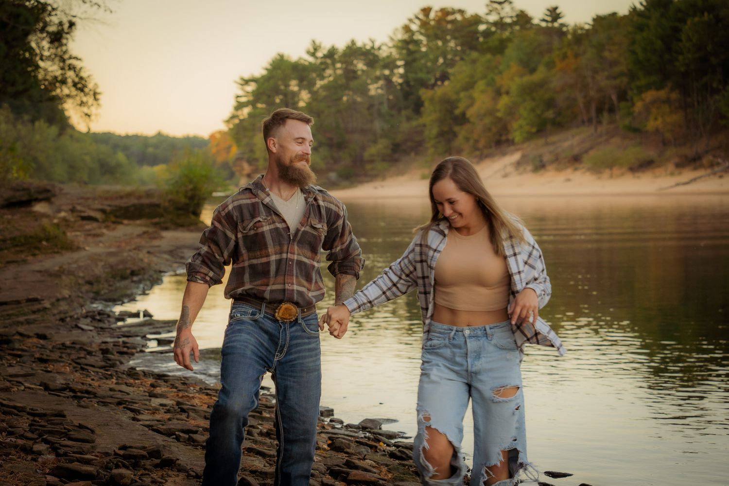 Wisconsin Couple and Engagement Photographer - Couple walking on riverbank in fall during engagement session in Wisconsin during sunset.