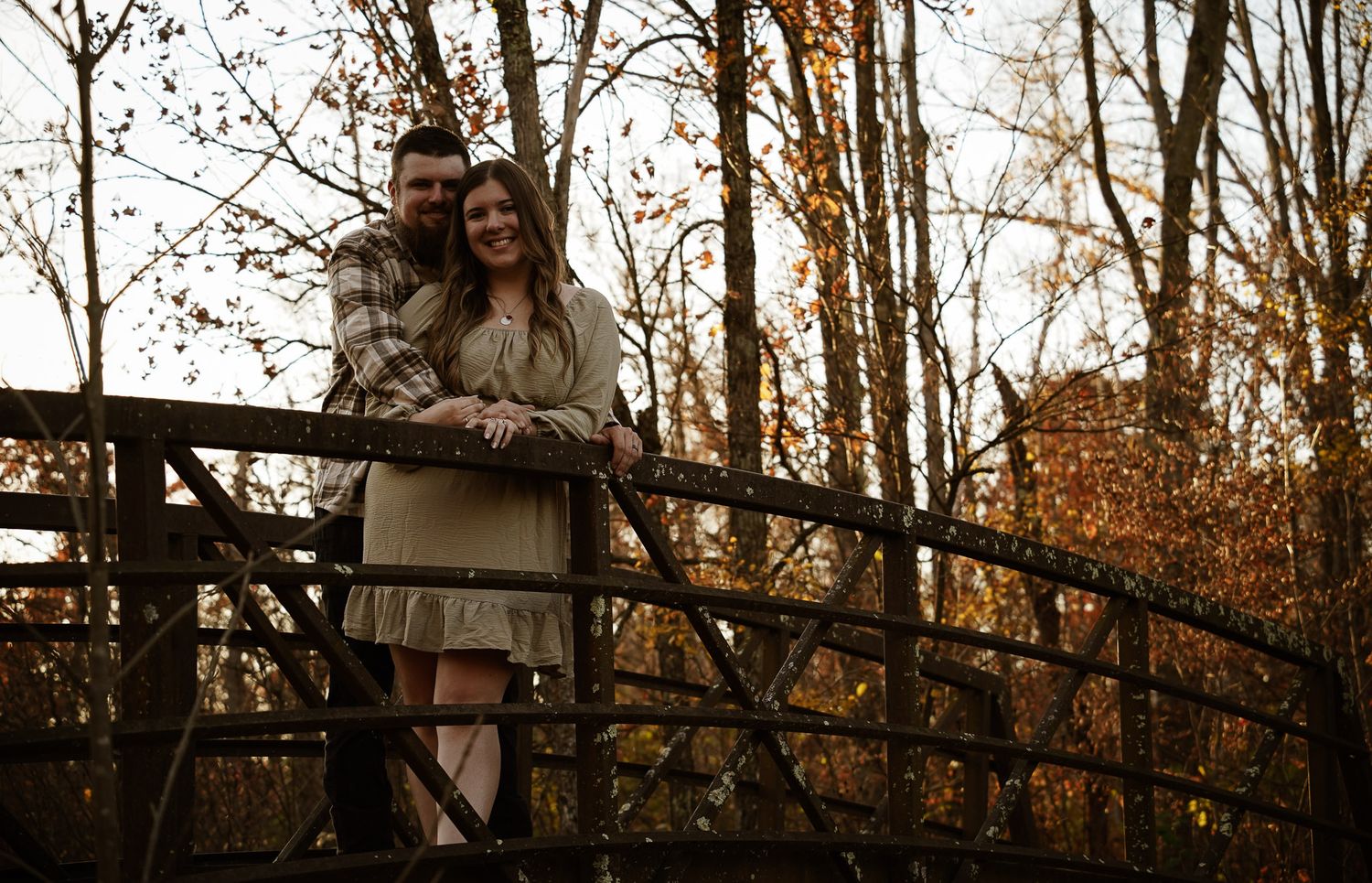 Wisconsin Couple and Engagement Photographer - Couple walking over bridge in woods in fall during an engagement session during sunset.