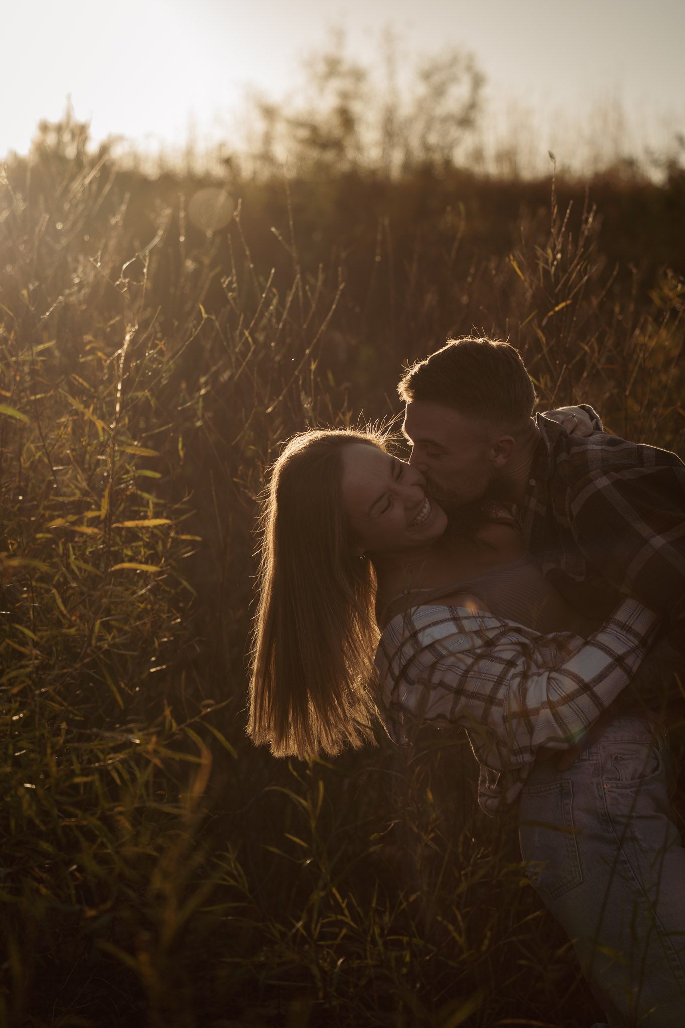 Wisconsin Couple and Engagement Photographer - Couple laughing in a field in fall during an engagement session in WI during sunset.
