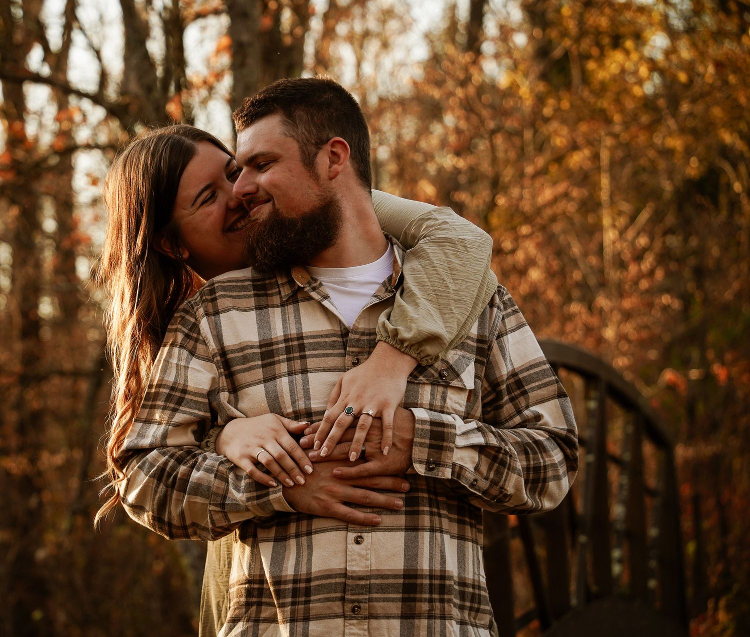 Wisconsin Couple and Engagement Photographer - Couple hugging over bridge in woods in fall during an engagement session during sunset.