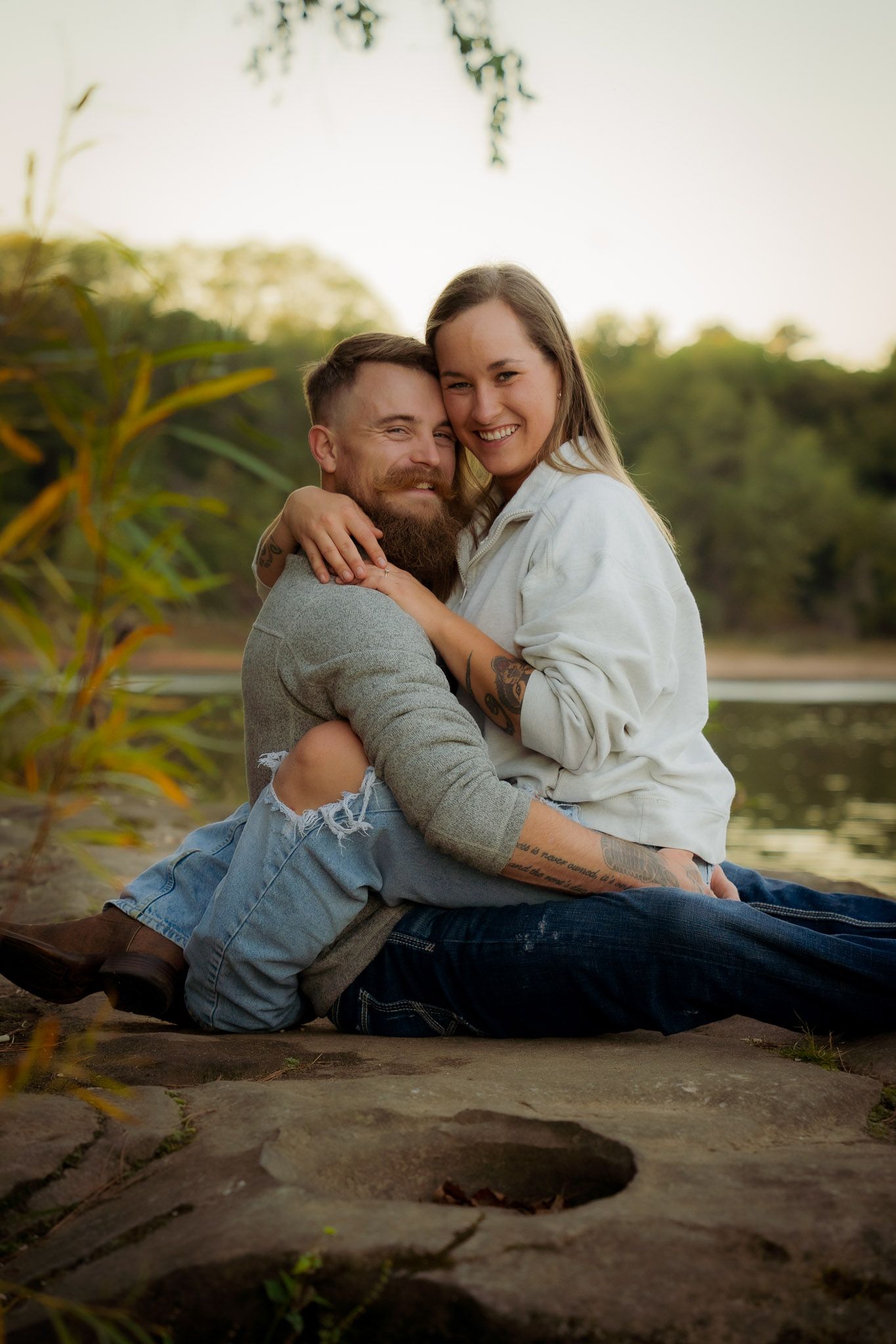 Wisconsin Couple and Engagement Photographer - Couple smiling on riverbank in fall during an engagement session in Wisconsin during sunset.