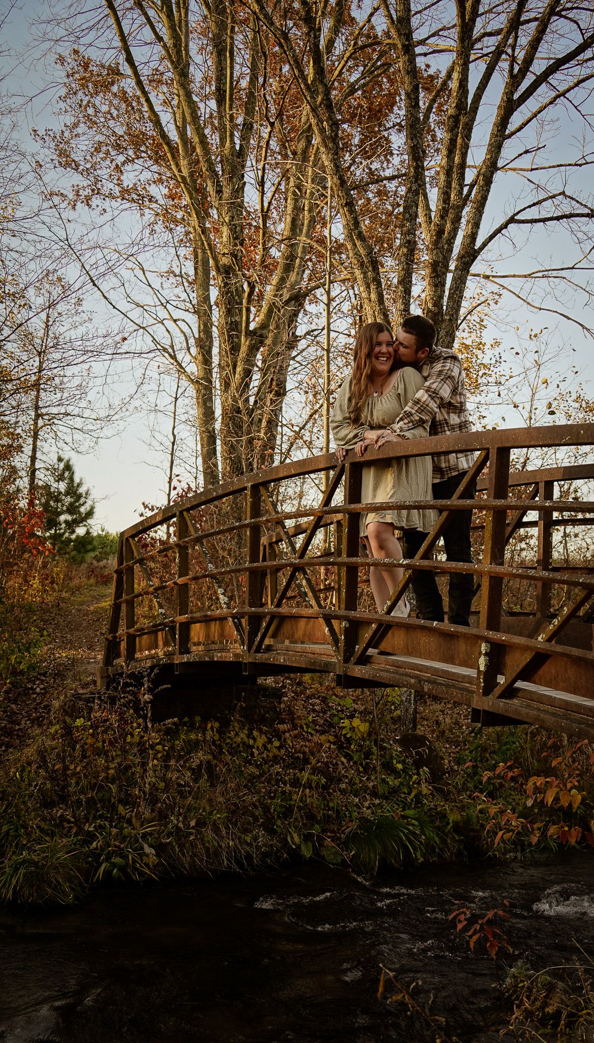 Wisconsin Couple and Engagement Photographer - Couple walking over bridge in woods in fall during an engagement session during sunset.