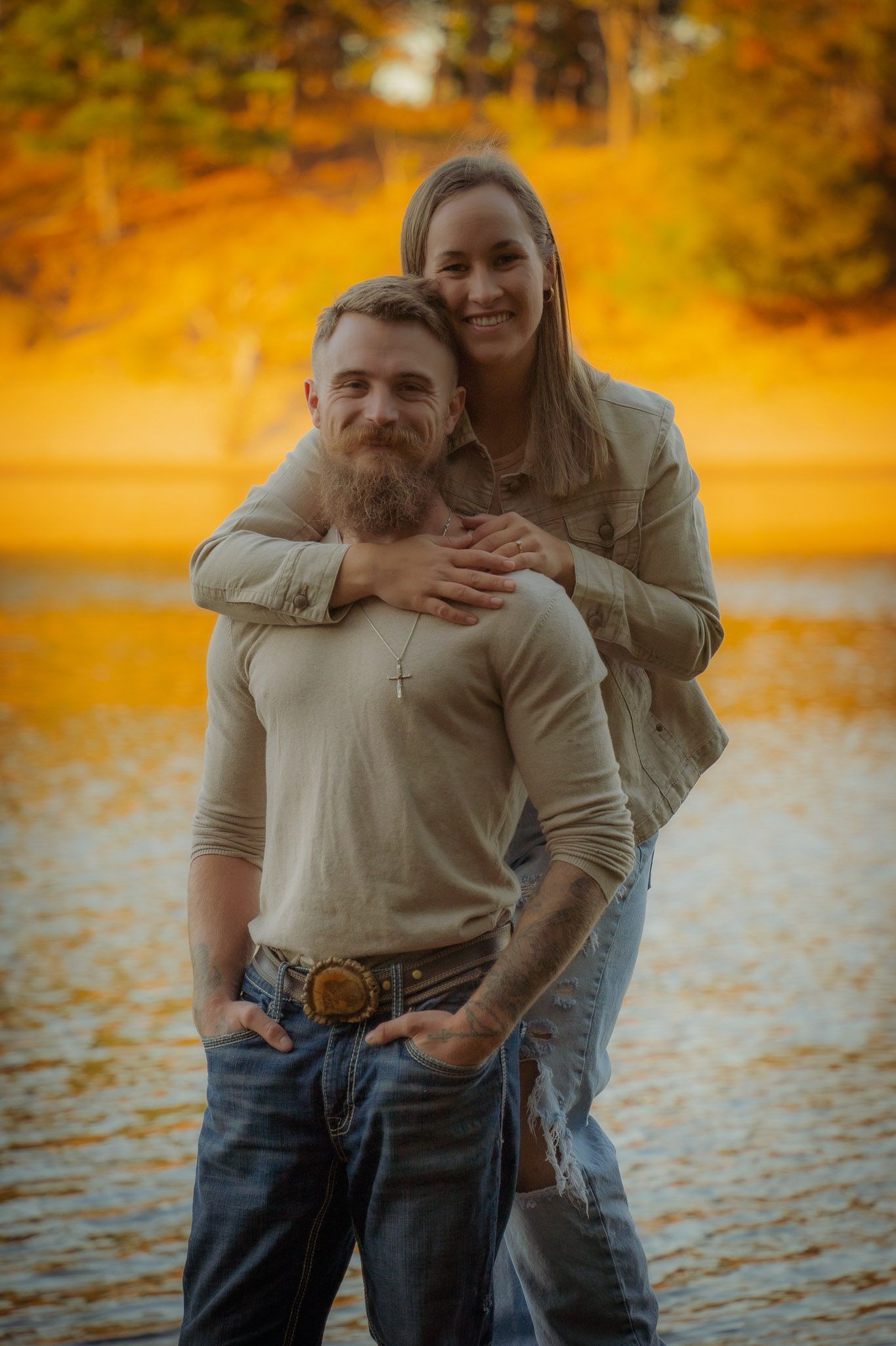 Wisconsin Couple and Engagement Photographer - Couple smiling on riverbank in fall during an engagement session in Wisconsin during sunset.