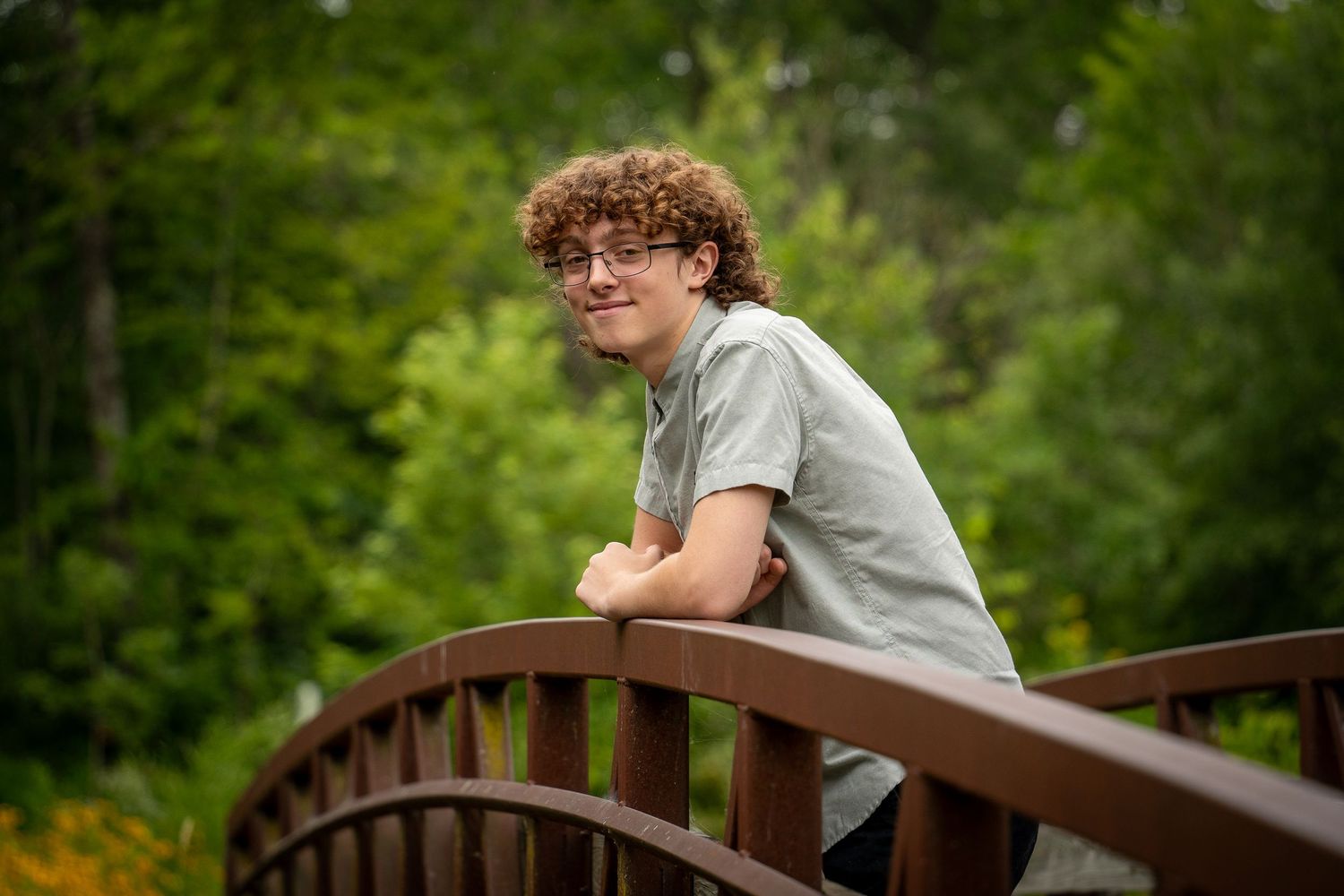 Wisconsin Senior and Portrait Photographer - Boy smiling on a bridge with yellow flowers in WI during a summer senior portrait session.