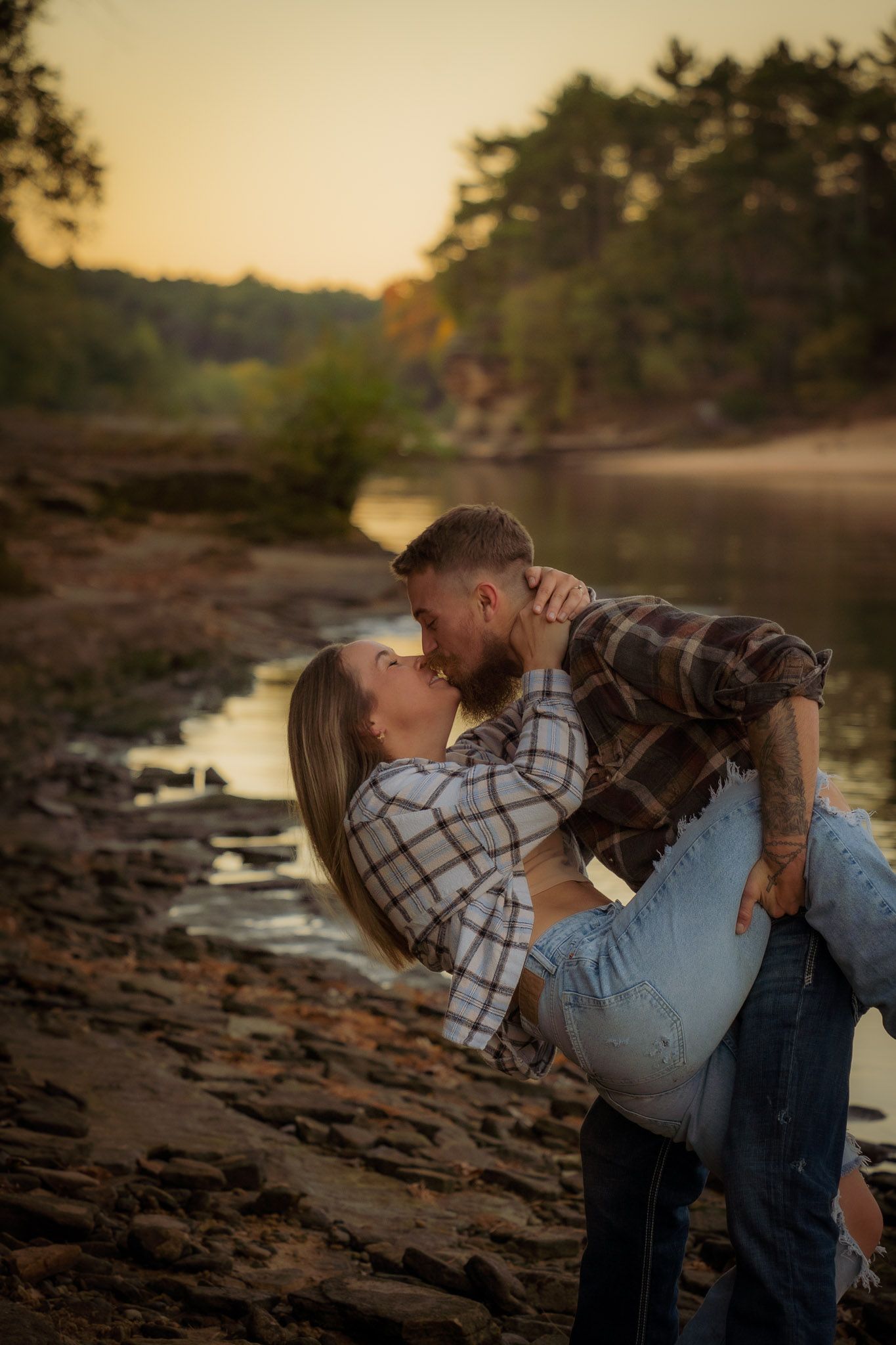 Wisconsin Couple and Engagement Photographer - Couple kissing on riverbank in fall during engagement session in Wisconsin during sunset.