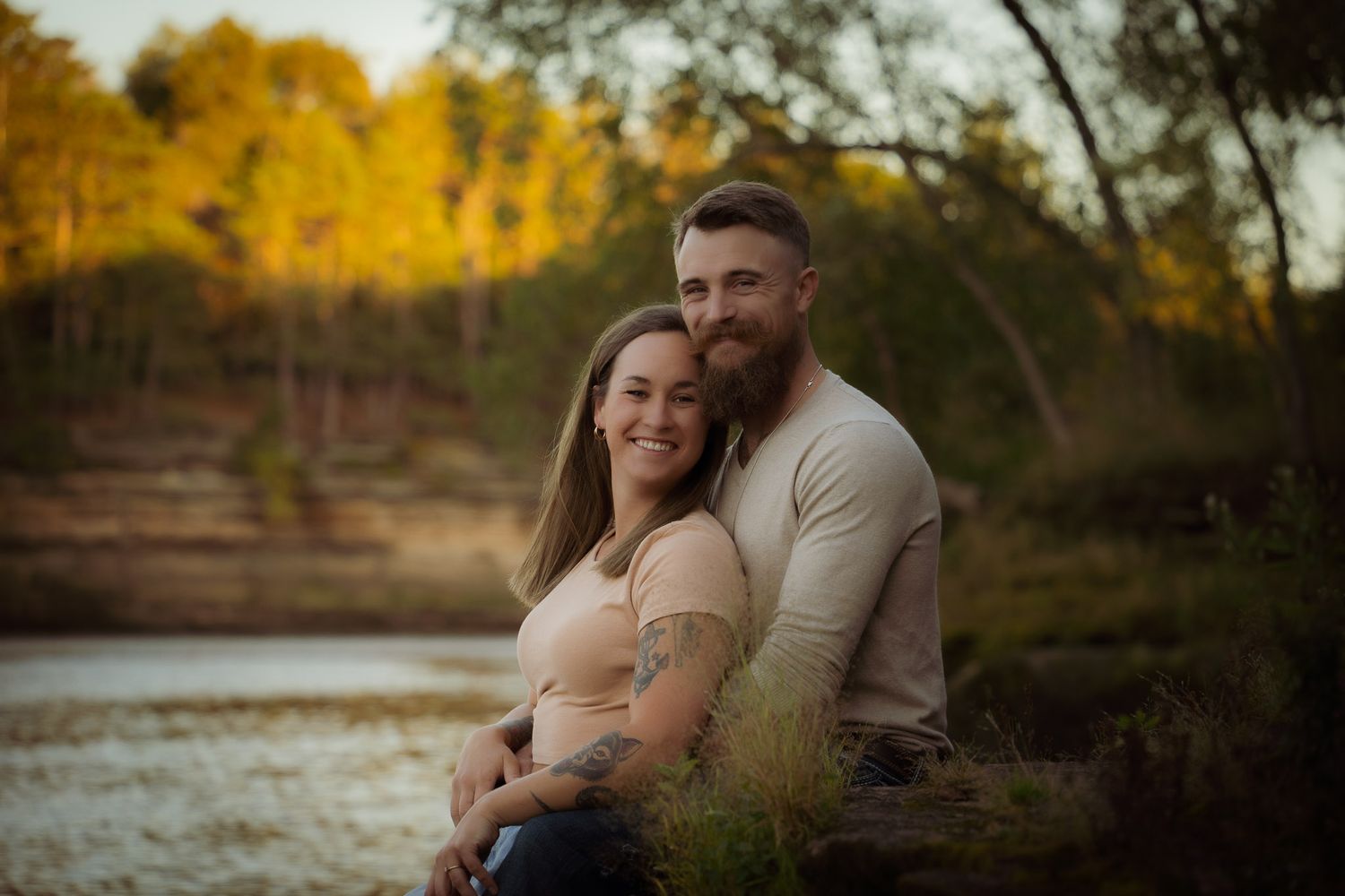 Wisconsin Couple and Engagement Photographer - Couple smiling on riverbank in fall during an engagement session in Wisconsin during sunset.