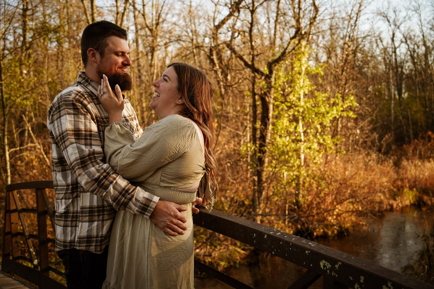 Wisconsin Couple and Engagement Photographer - Couple smiling on bridge in woods in fall during an engagement session during sunset.