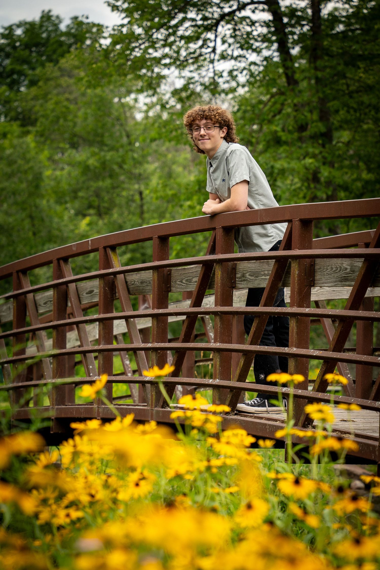 Wisconsin Senior and Portrait Photographer - Boy smiling on a bridge with yellow flowers in WI during a summer senior portrait session.