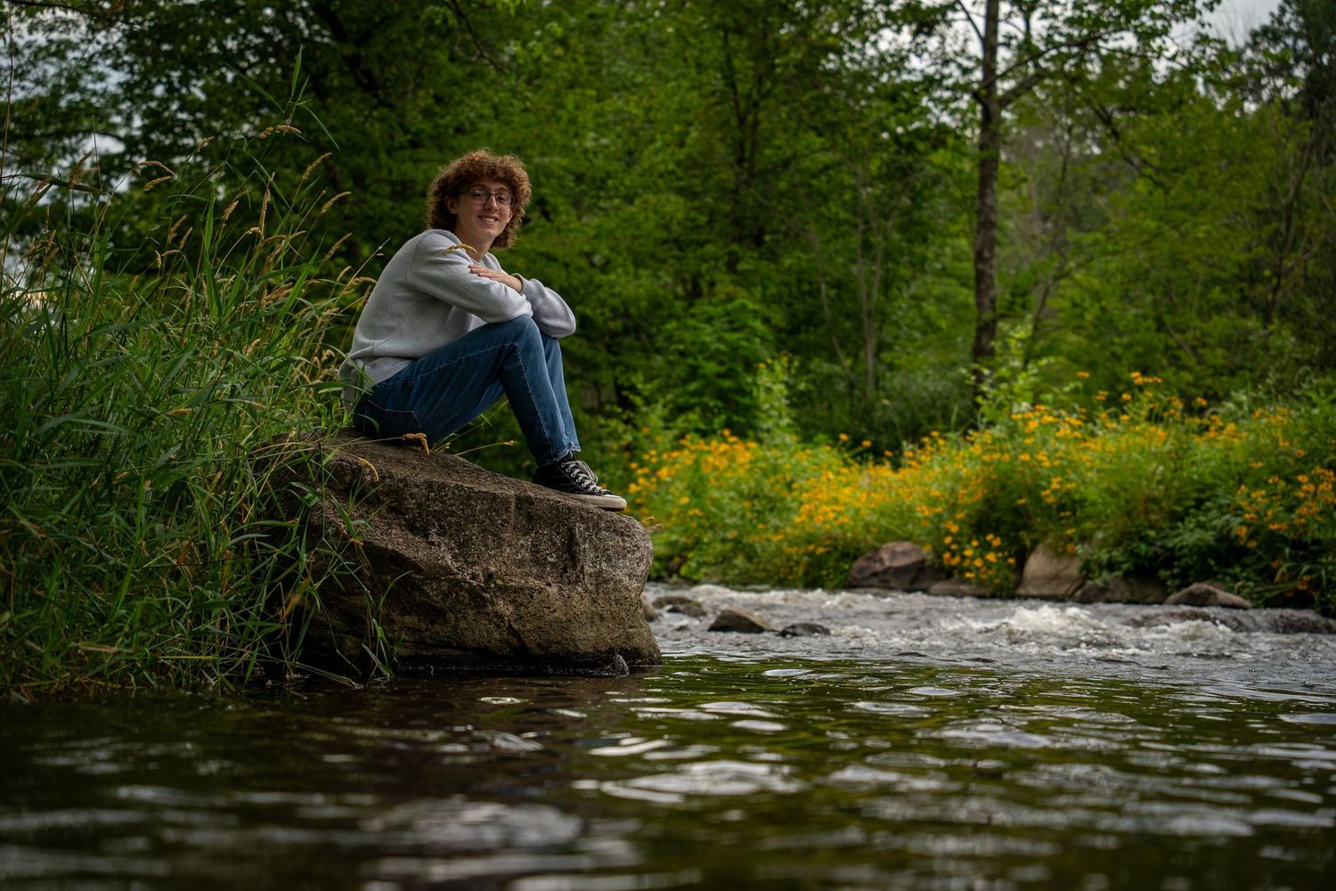 Wisconsin Senior and Portrait Photographer - Boy sitting on a rock on river smiling in Wisconsin during a summer senior portrait session.