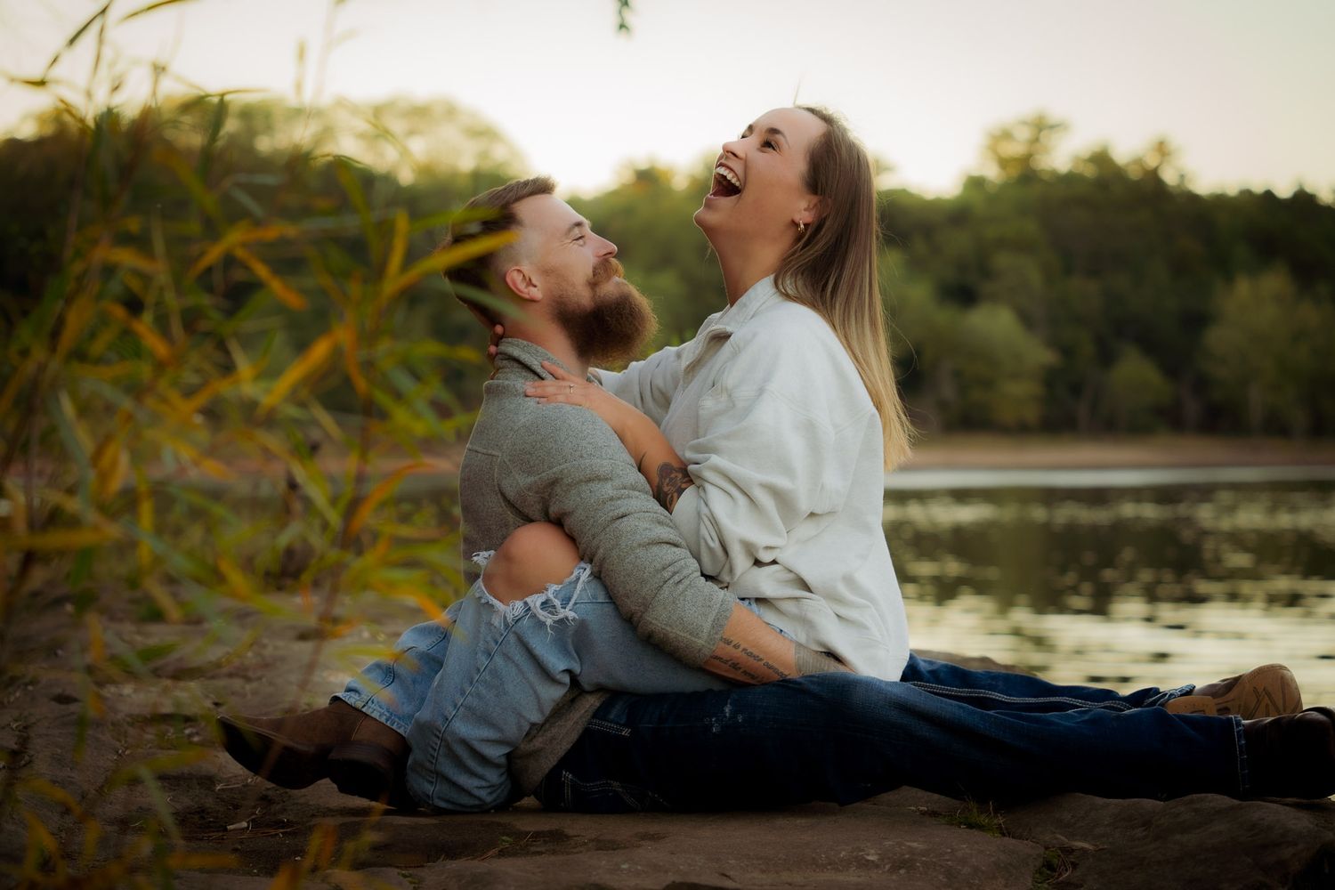 Wisconsin Couple and Engagement Photographer - Couple laughing on riverbank in fall during engagement session in Wisconsin during sunset.