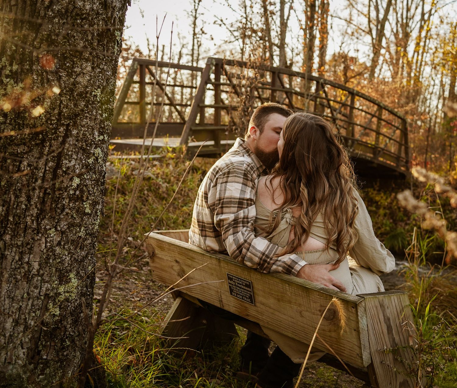 Wisconsin Couple and Engagement Photographer - Couple kissing near bridge in woods in fall during an engagement session during sunset.