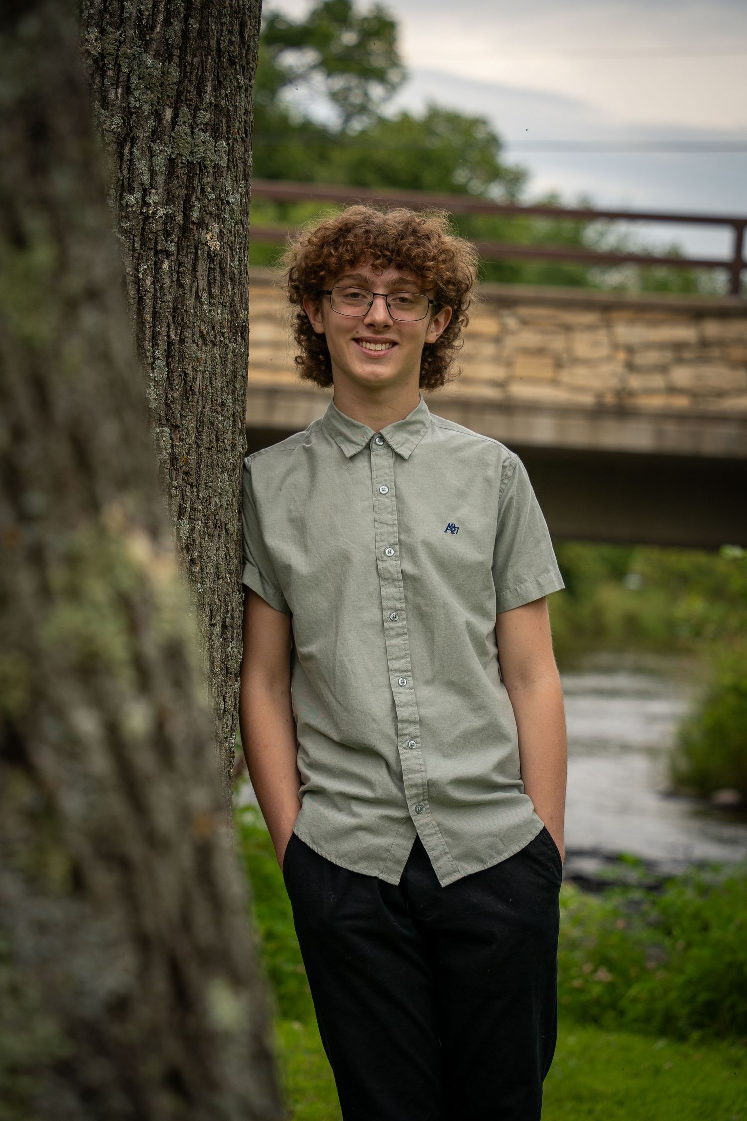 Wisconsin Senior and Portrait Photographer - Boy leaning on a tree next to a bridge in Wisconsin during a summer senior portrait session.