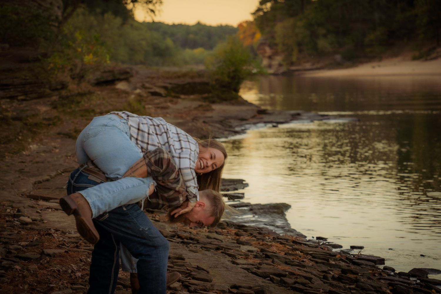 Wisconsin Couple and Engagement Photographer - Couple laughing on riverbank in fall during engagement session in Wisconsin during sunset.