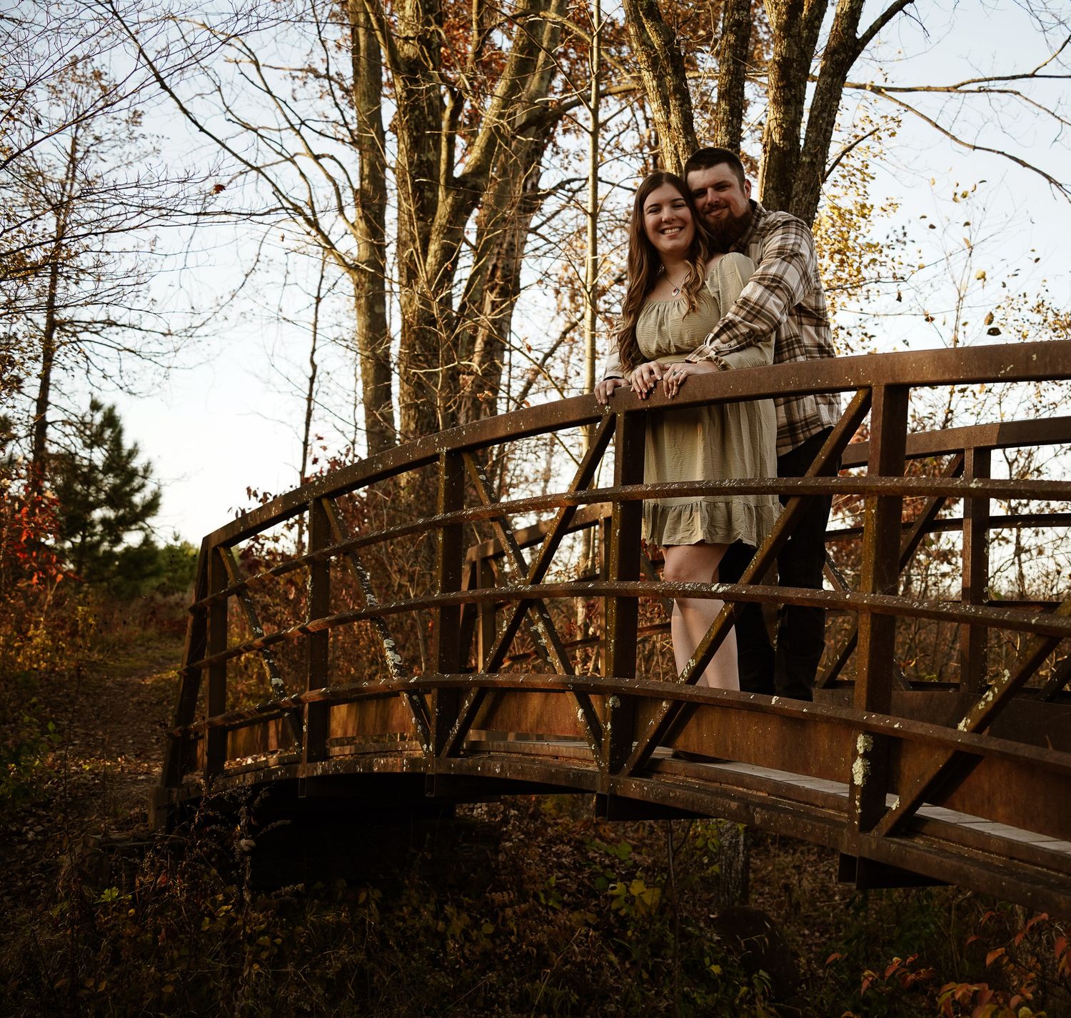 Wisconsin Couple and Engagement Photographer - Couple walking over bridge in woods in fall during an engagement session during sunset.