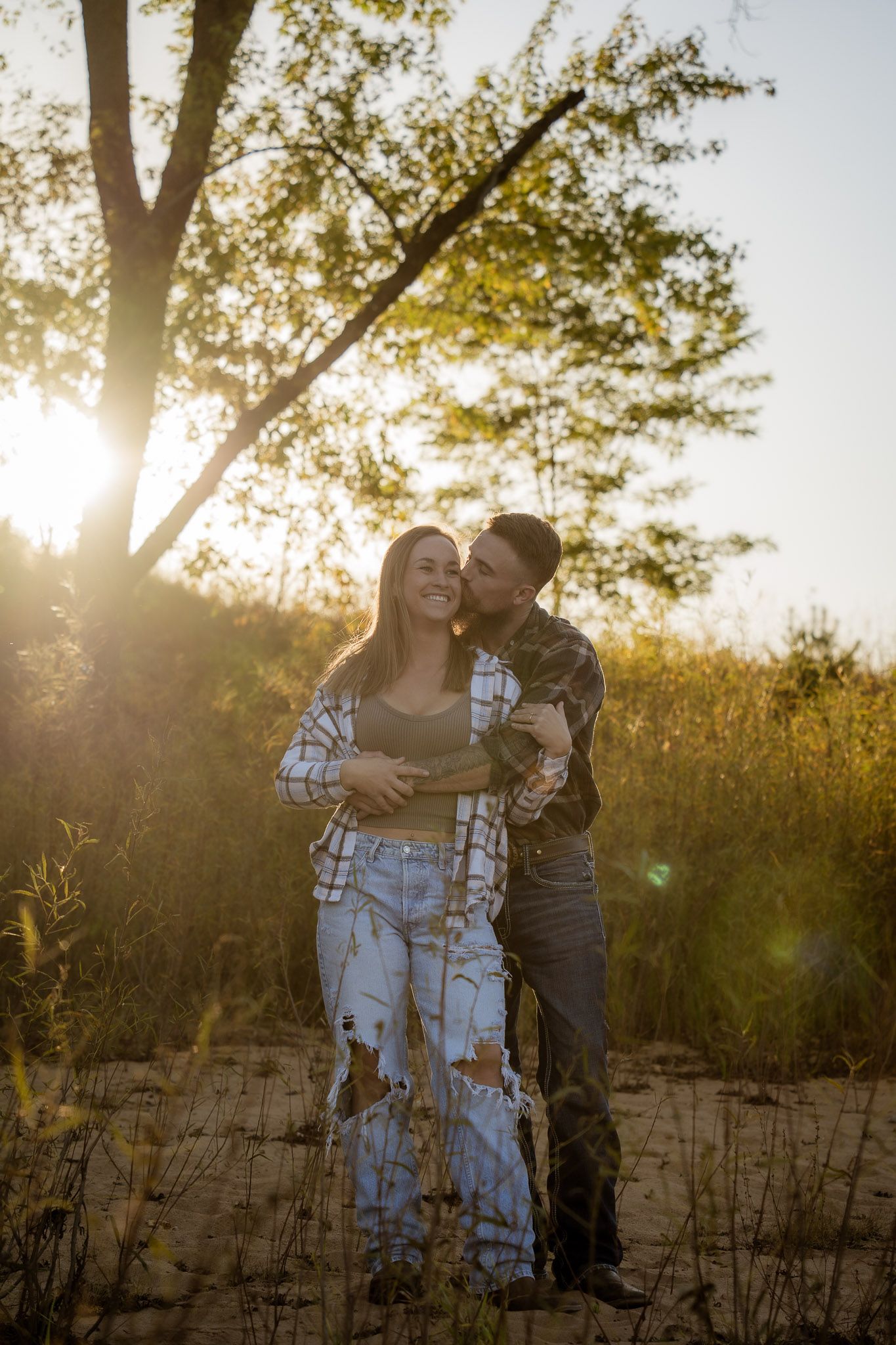 Wisconsin Couple and Engagement Photographer - Couple laughing on a beach in fall during an engagement session in Wisconsin during sunset.