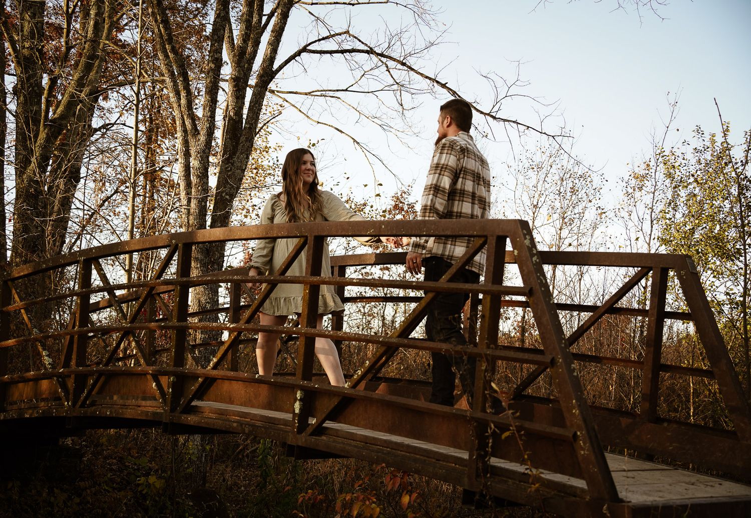 Wisconsin Couple and Engagement Photographer - Couple walking over bridge in woods in fall during an engagement session during sunset.