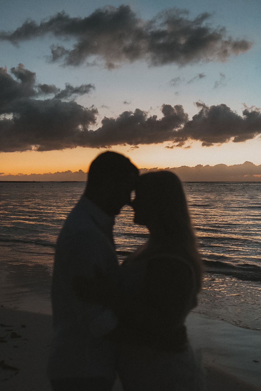 Silhouettes against a dramatic beach sunset with orange and purple clouds over the ocean in Secrets Akumal Mexico
