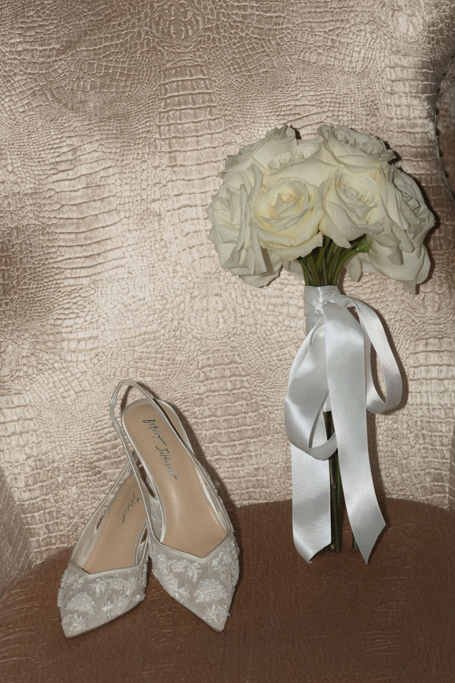 White bridal shoes and bouquet of roses arranged against textured background details at Le Venere wedding venue in Saint Paul Minnesota