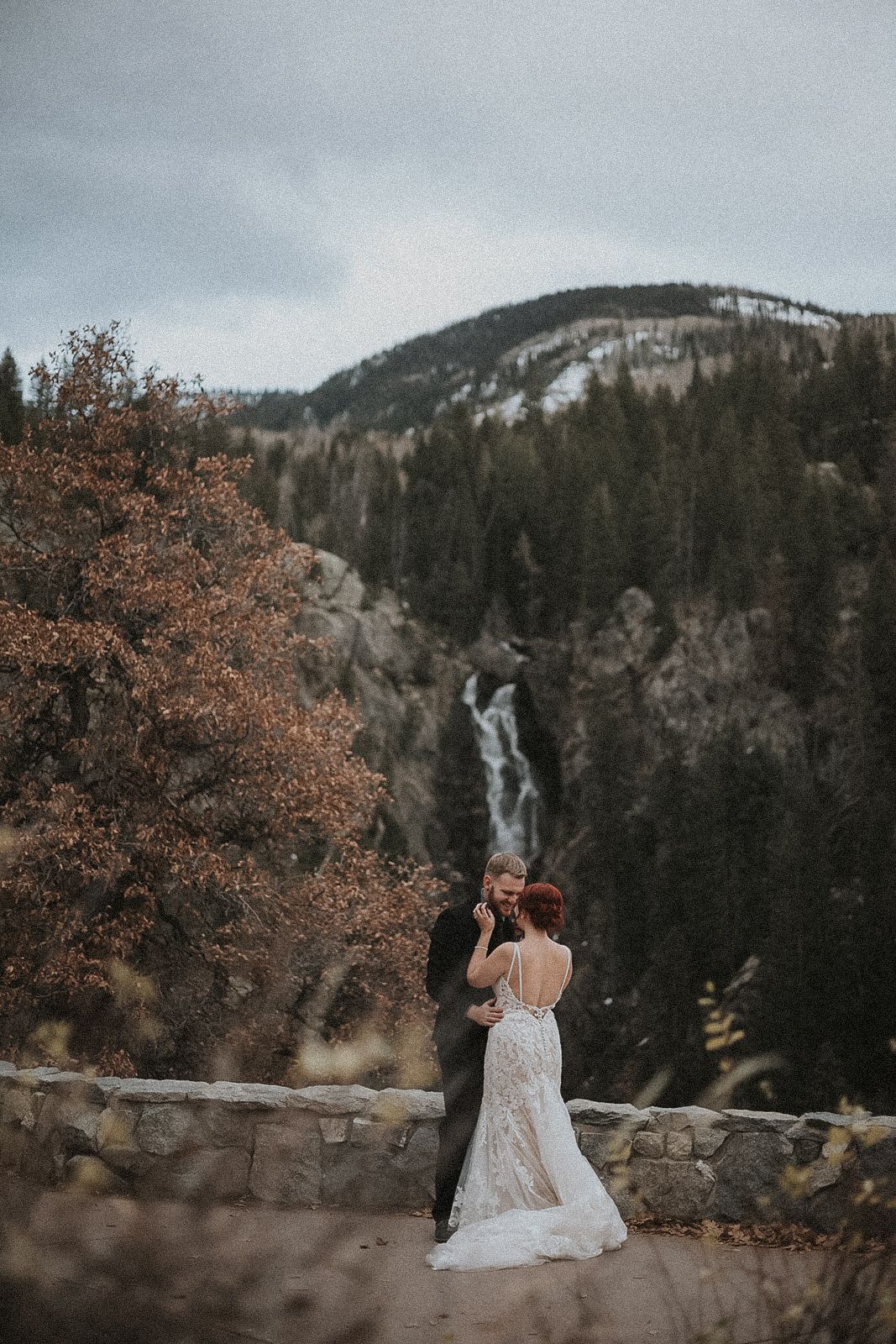 A married couple sits together on a stone wall overlooking a scenic mountain landscape in Colorado