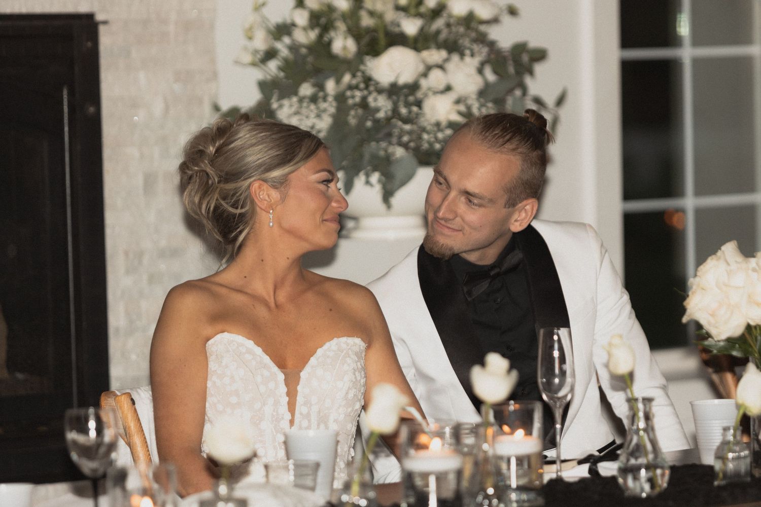 An intimate reception dinner moment with elegant table settings and white floral decor. Bride & Groom share a sweet glance at Abella Wedding
