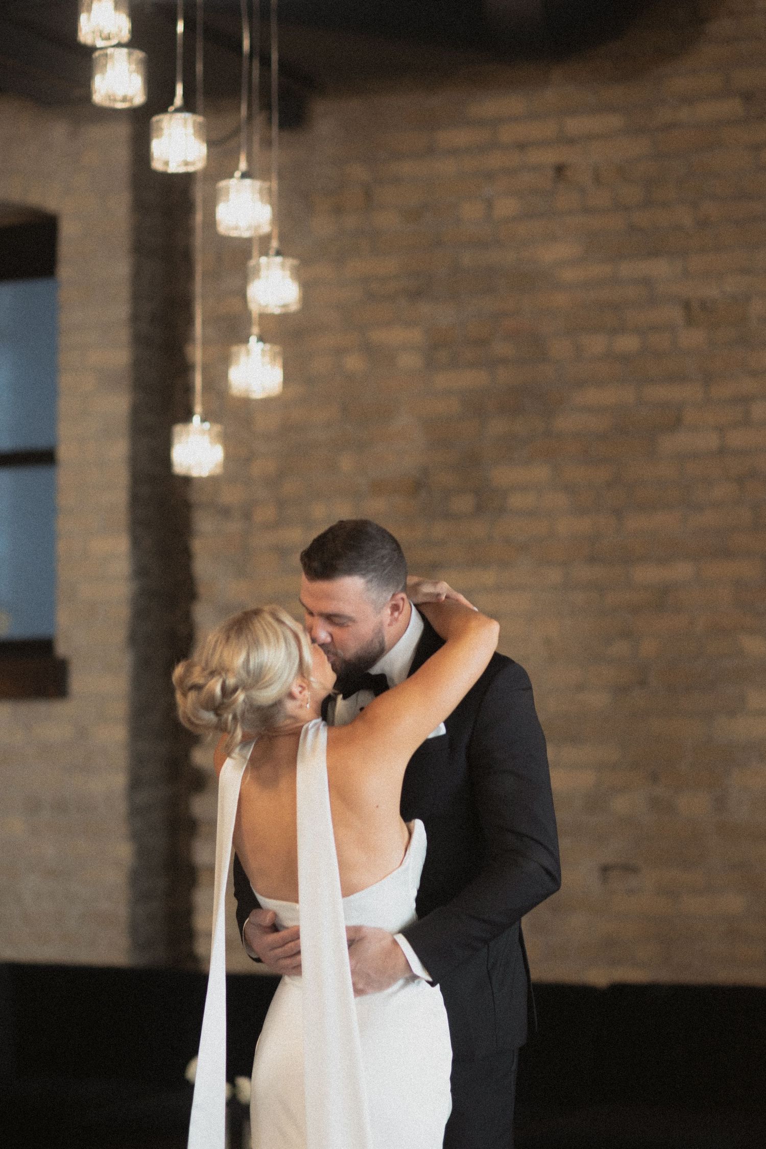 Romantic bride and groom dancing and kissing in industrial Le Venere wedding venue in Saint Paul Minnesota with hanging lights.
