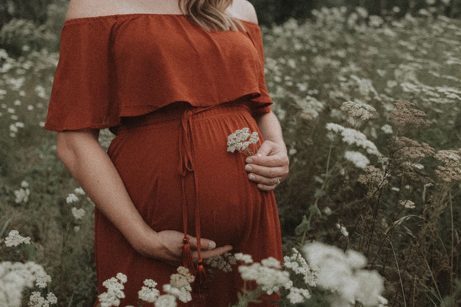 Maternity photos in a rustic outdoor setting with white wildflowers and a rust-colored dress.